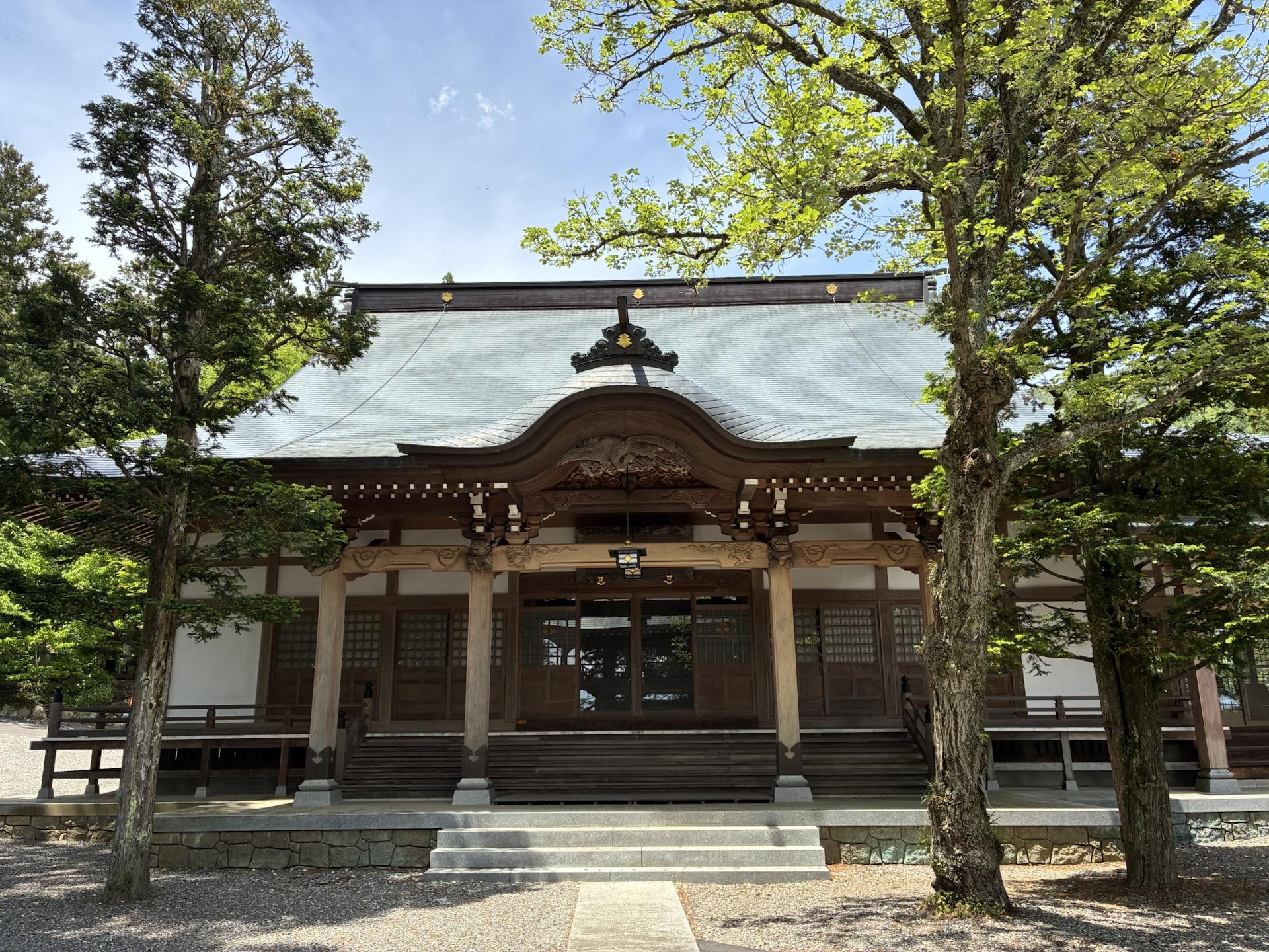 金松寺の本堂。瓦屋根の立派な建物の前に石畳の参道が伸び、両脇に大きな木が立っている。空は快晴