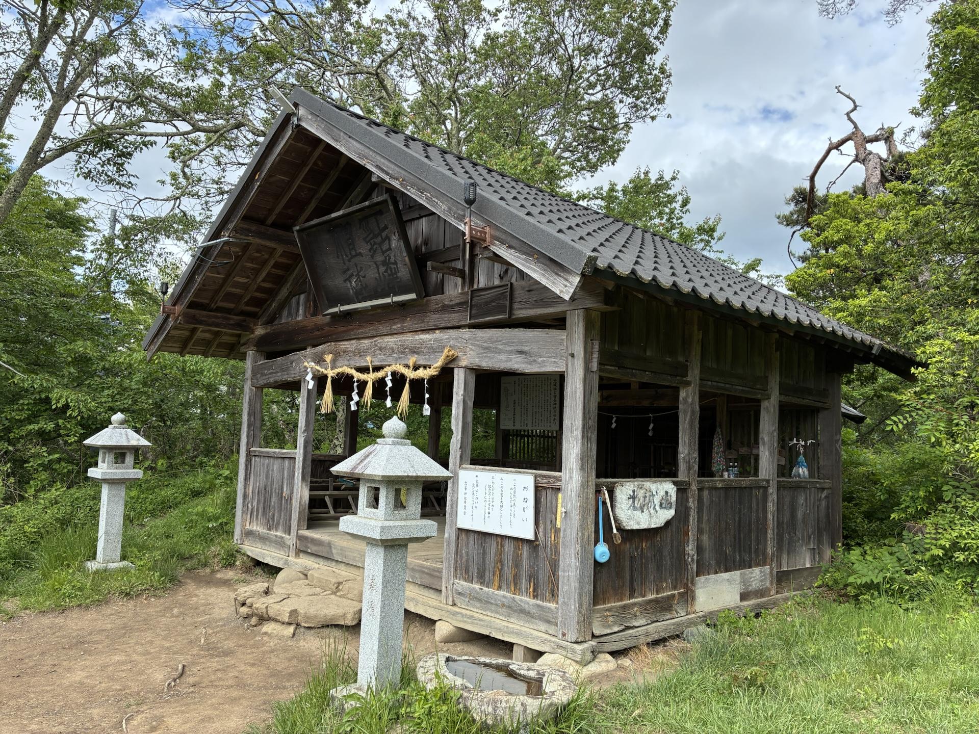 光城山山頂に建つ古峯神社の社殿。木造の小さなお堂の前に石灯籠が並び、周囲は新緑の木々に囲まれている