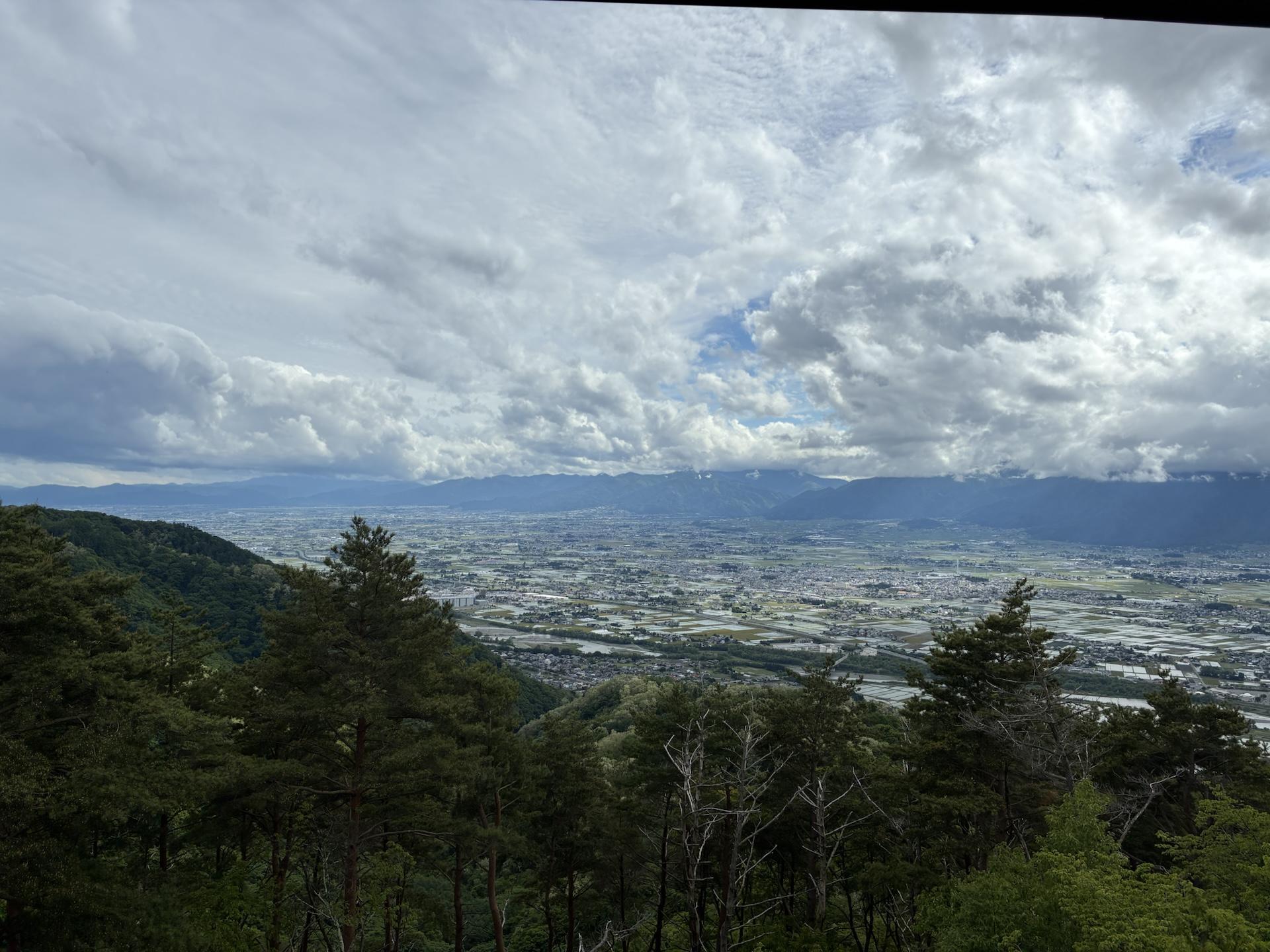 長峰山から南を見た眺め。眼下に松本平の街並みが広がり、遠くの山並みの上に厚い雲がかかっている