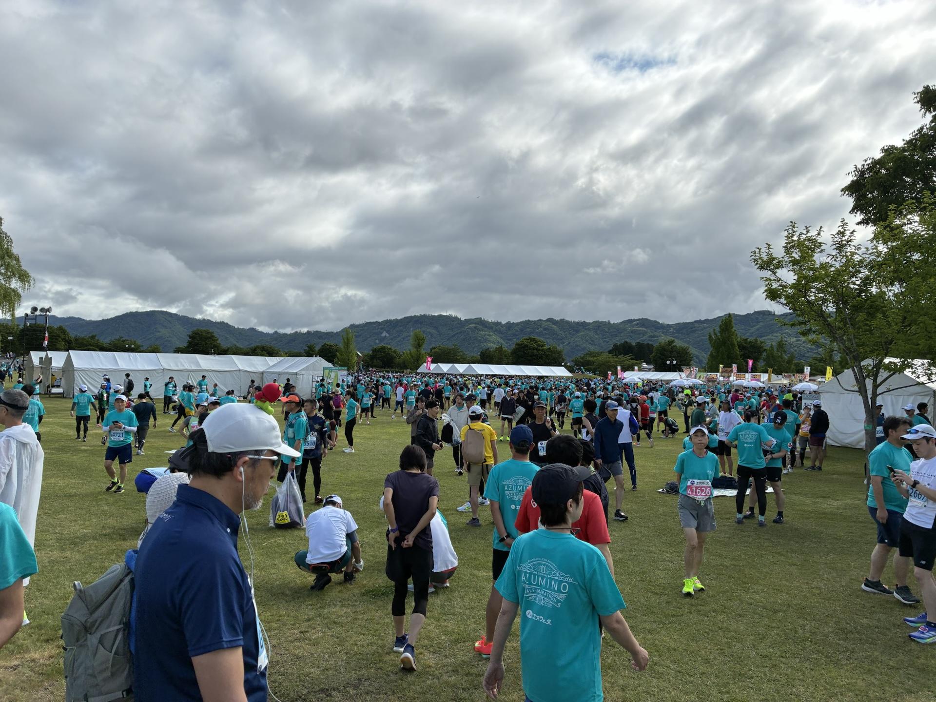 大会会場の芝生広場。おそろいの水色のTシャツを着たランナーが大勢集まり、奥にはテントと山並みが見えている