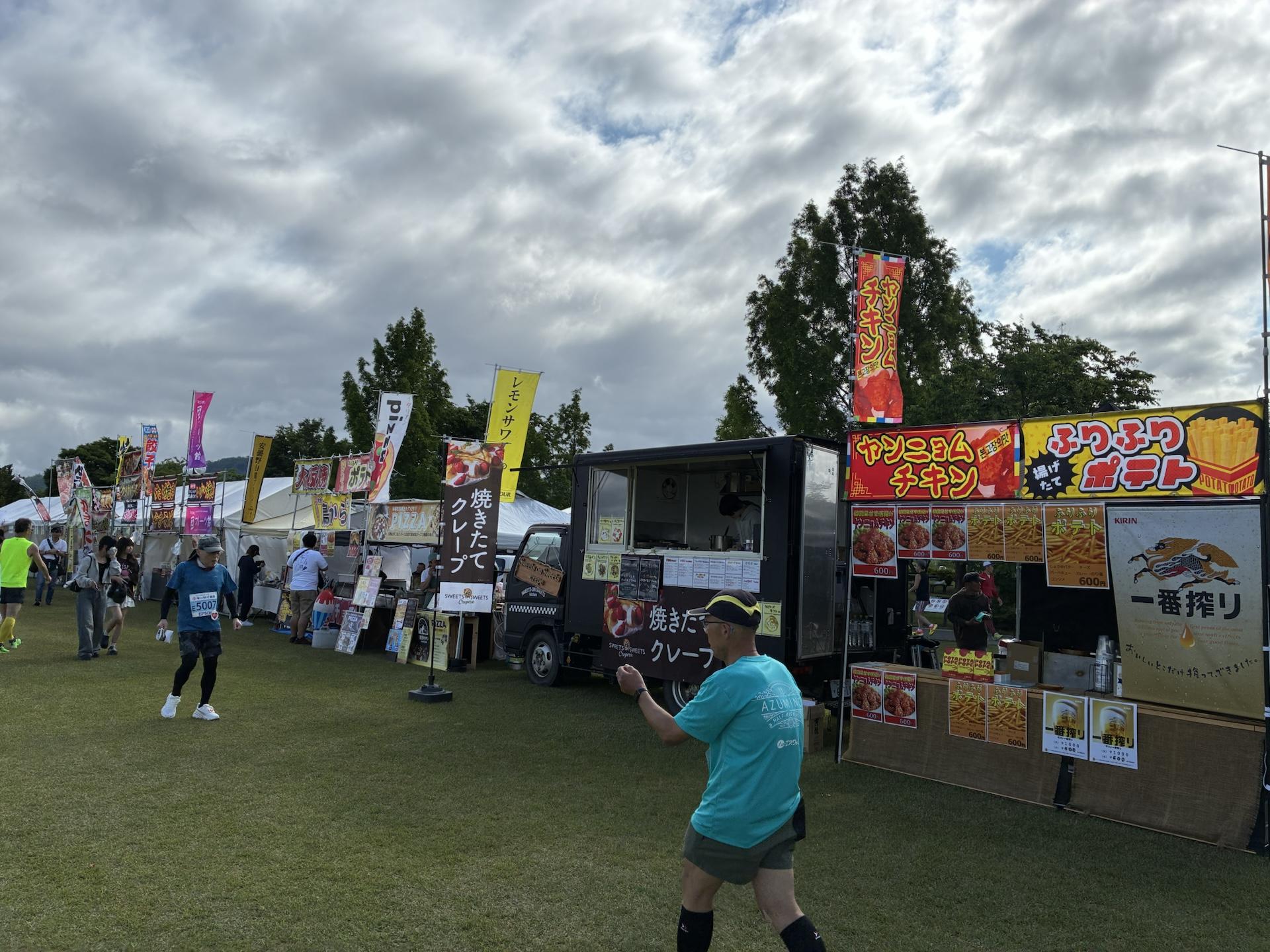 会場に並ぶキッチンカーと出店。からあげやクレープののぼりが立ち、その前を参加者が歩いている