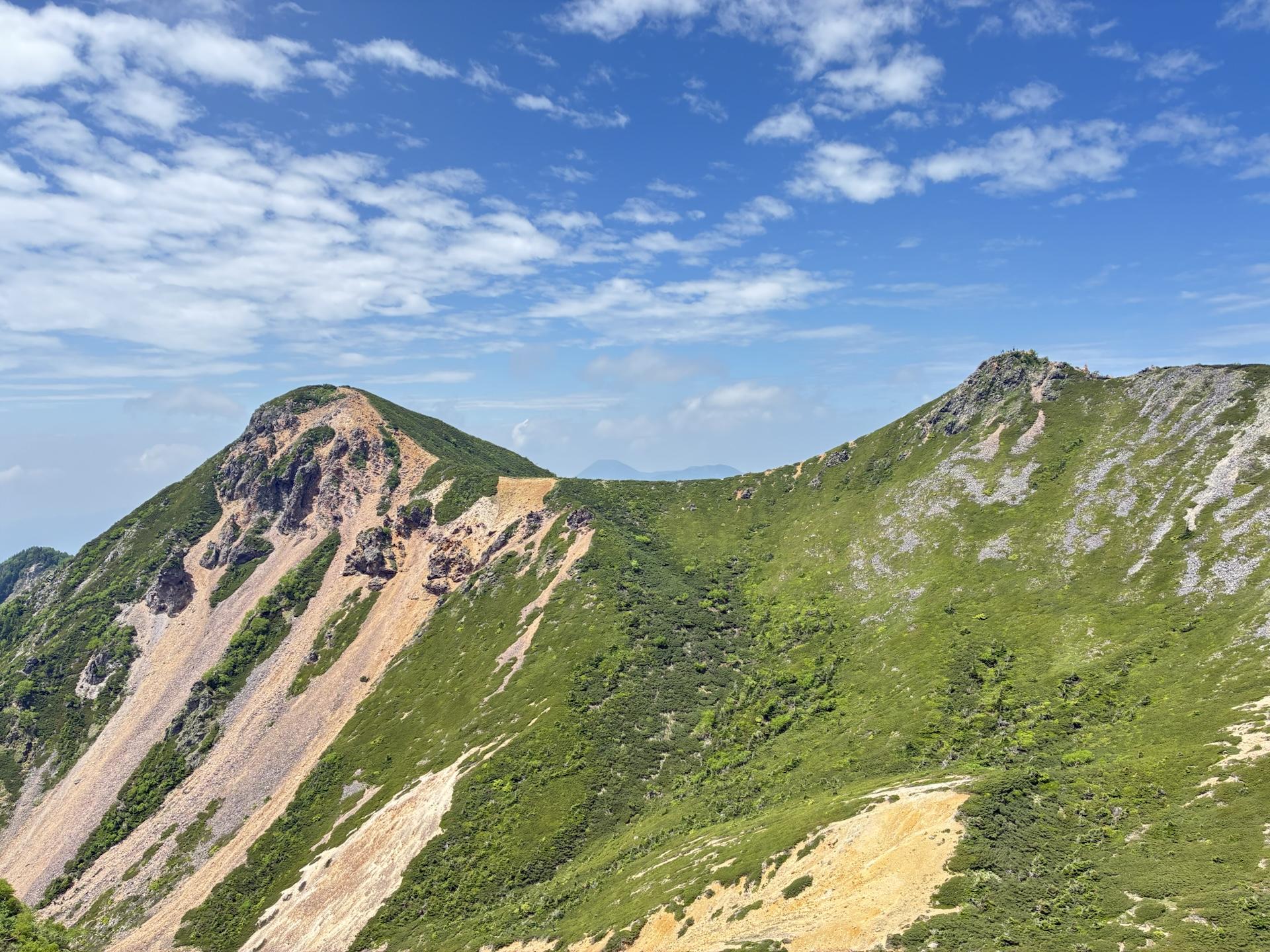 根石岳から見た東天狗岳と西天狗岳。二つのピークをつなぐ稜線が弧を描いて伸び、青空と白い雲が背景に広がる