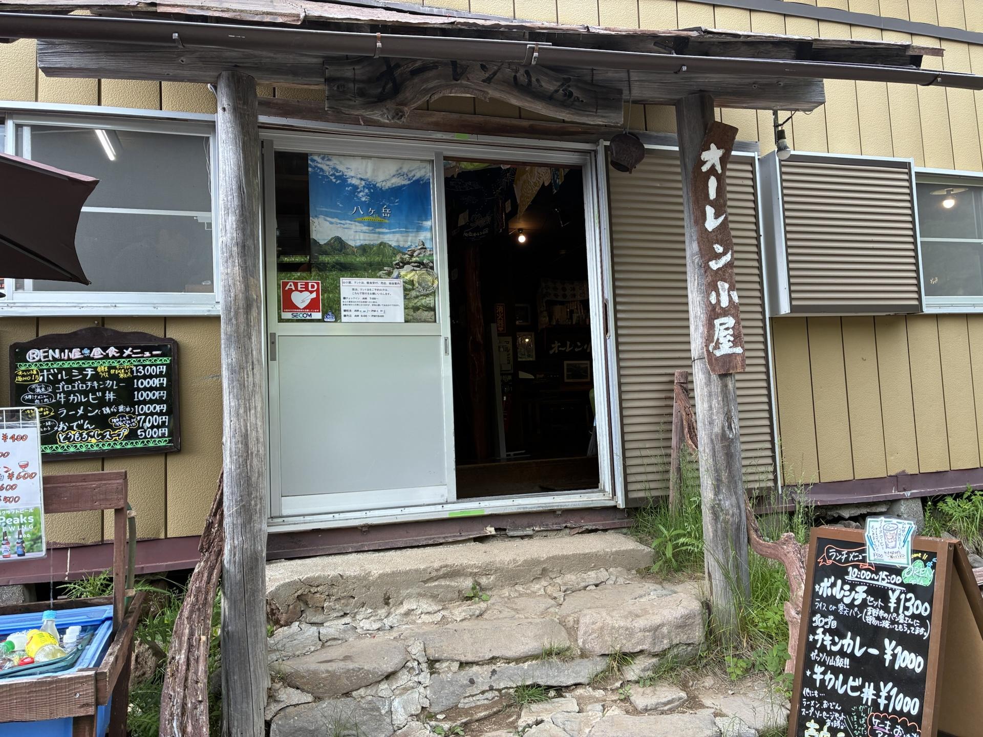 樹林に囲まれたオーレン小屋。木造の建物の前にタルチョーのような色とりどりの旗が張られている