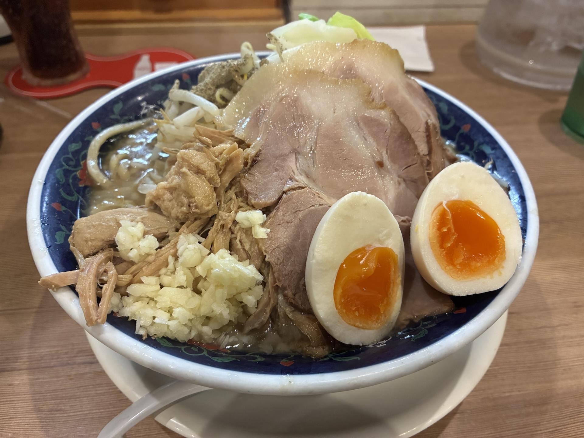 どんぶりに盛られた二郎系ラーメン。厚切りのチャーシューと半熟の味玉、刻みニンニクが乗っている