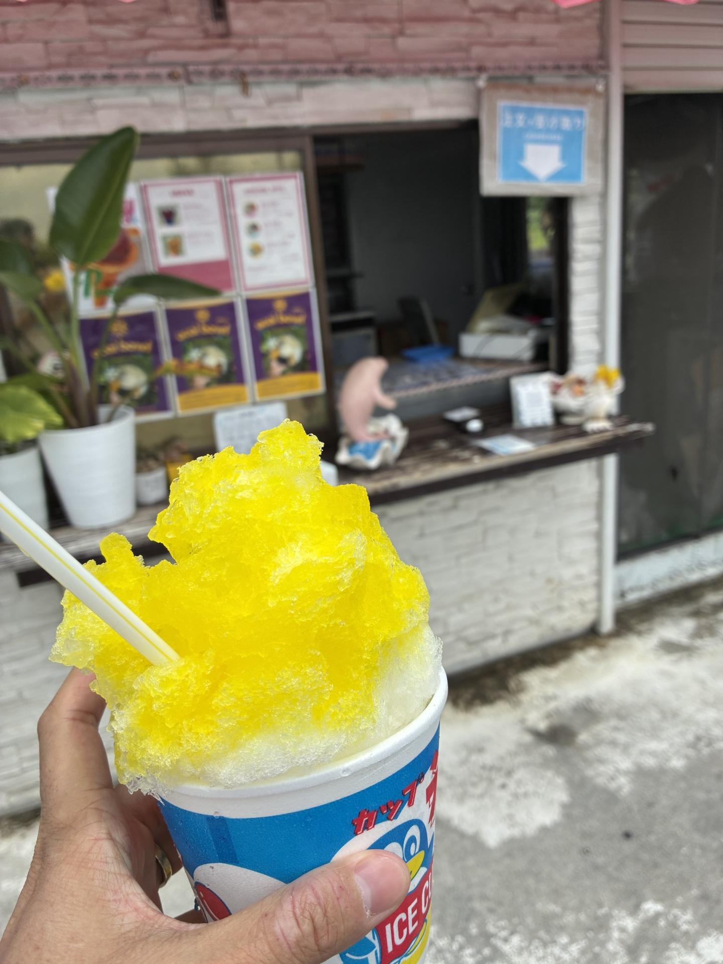 カップに山盛りになった黄色いレモンのかき氷。ストローが刺さっていて、後ろには店のカウンターが写っている