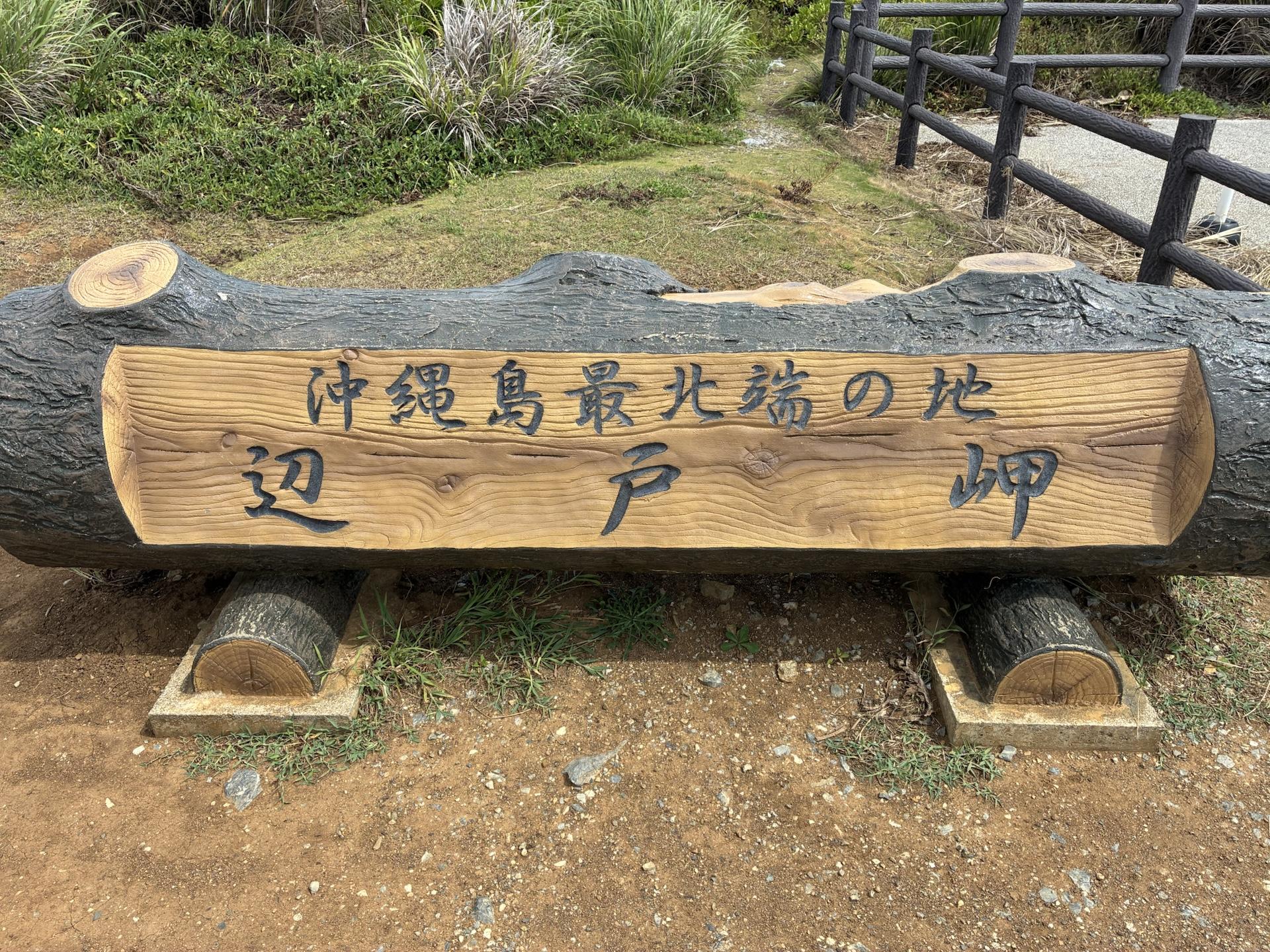「沖縄島最北端の地 辺戸岬」と彫られた大きな木の看板。背景は岬の緑と柵