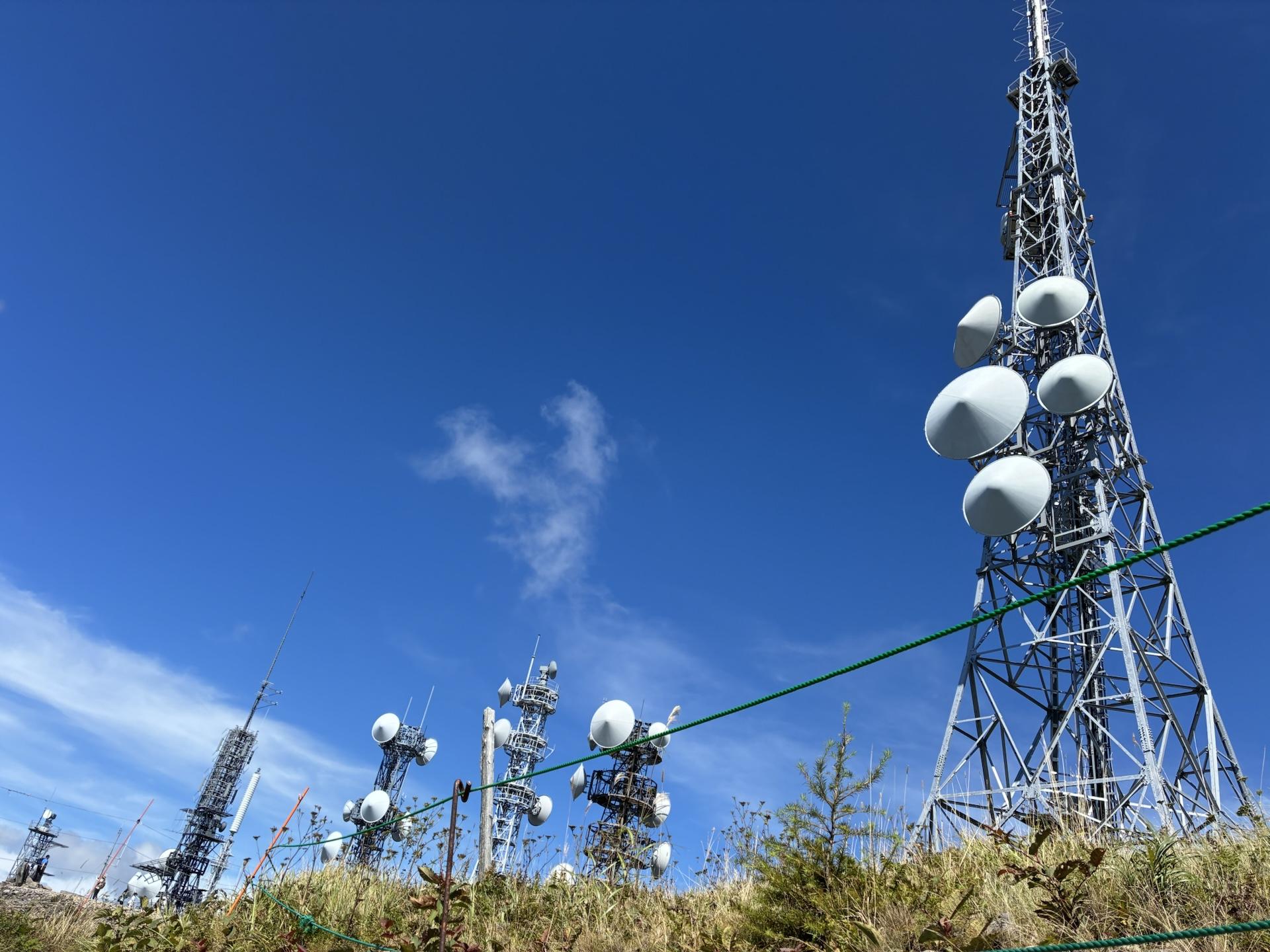 青空に向かって伸びる王ヶ頭の電波塔群。パラボラアンテナが付いた鉄塔が何本も並び立っている