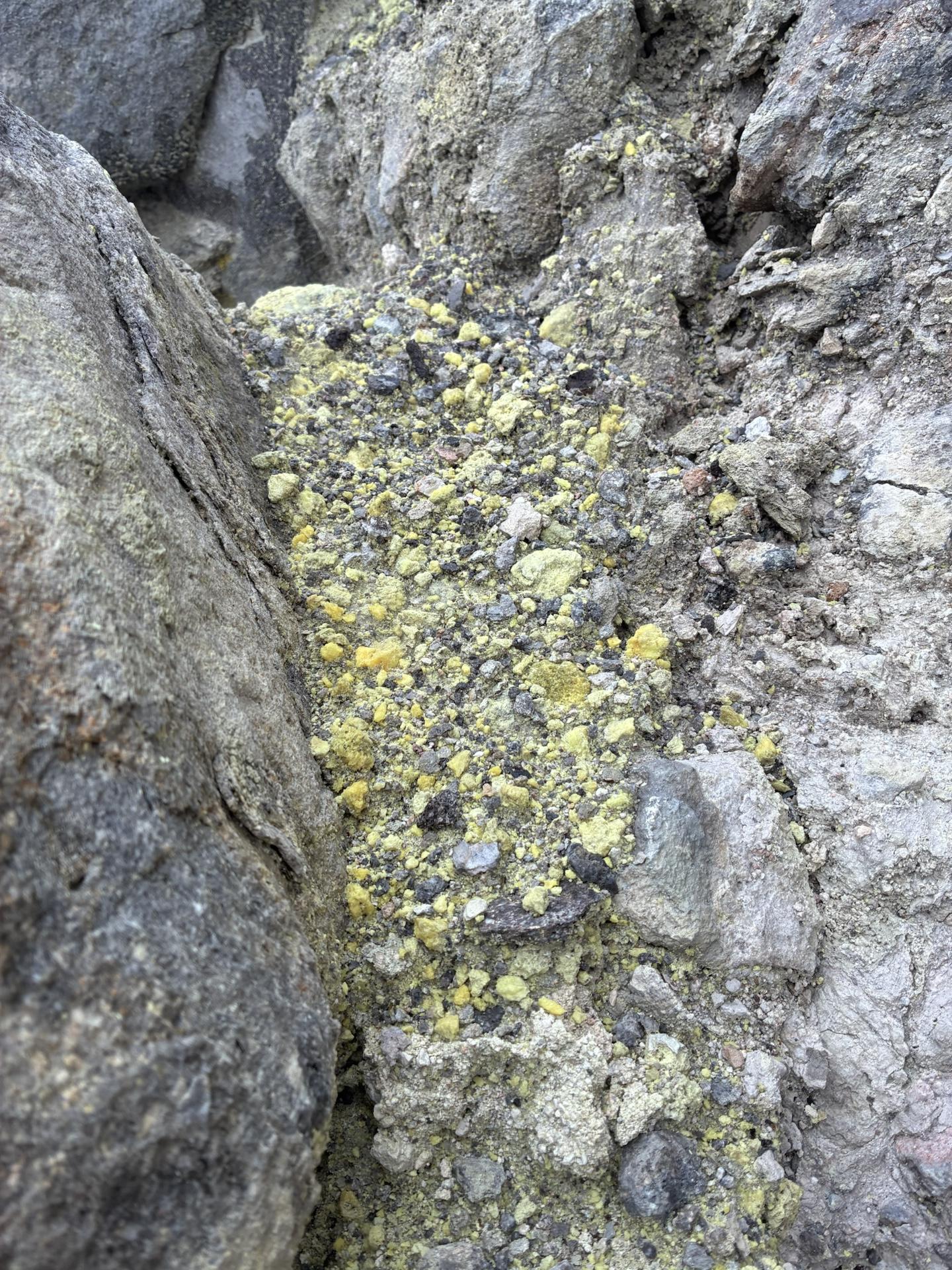 岩の隙間に堆積した黄色い硫黄。灰色の岩肌との対比で、黄色い粒がはっきり見える