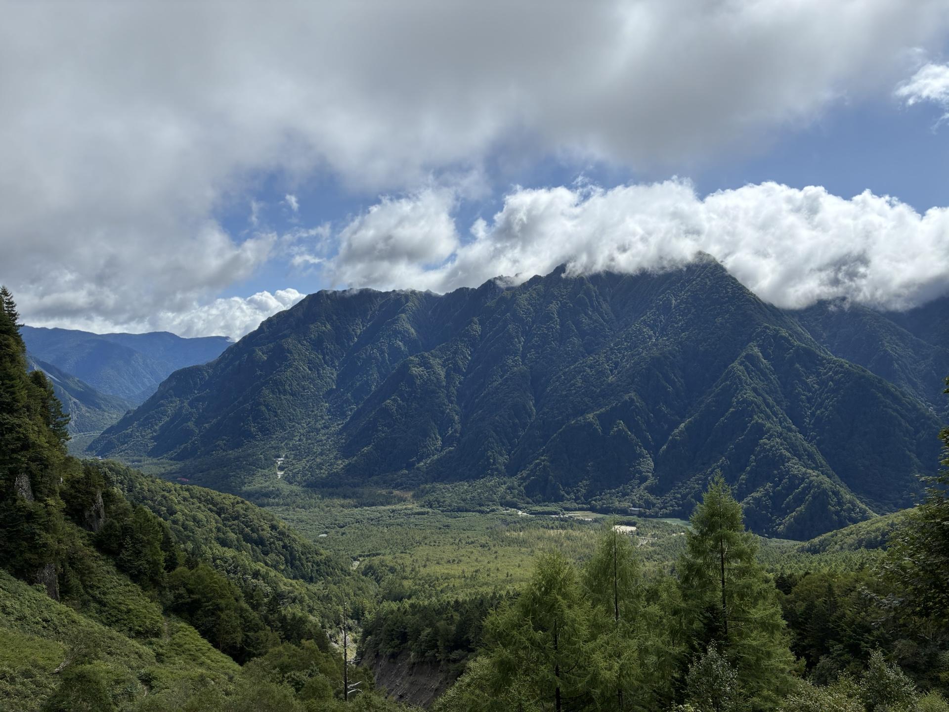 上高地の谷を挟んで対岸にそびえる霞沢岳。稜線に雲がかかり、眼下には梓川沿いの緑の谷が広がっている