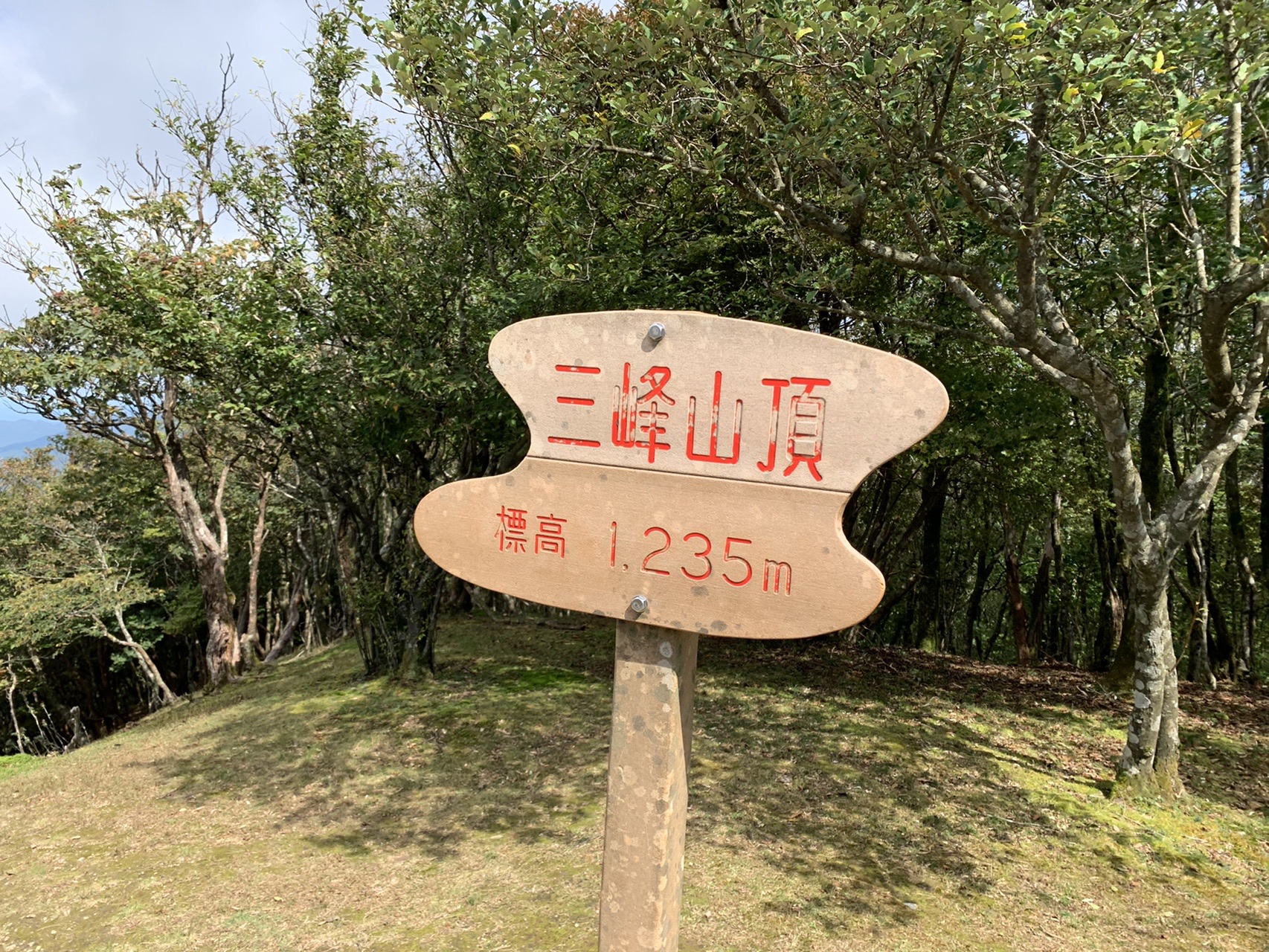 三峰山の山頂標柱。「三峰山頂 標高1,235m」と赤い文字で書かれた木の標識