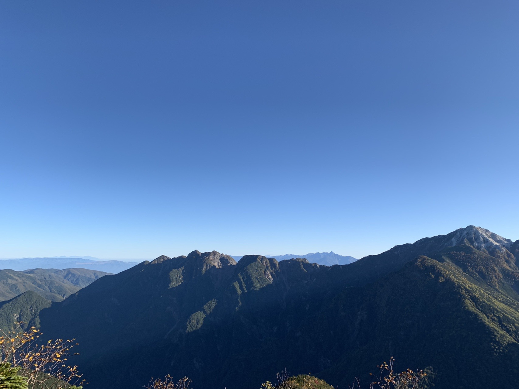 朝の稜線から見渡す山並み。手前の尾根がシルエットになり、奥まで山が重なっている。空は澄んだ青