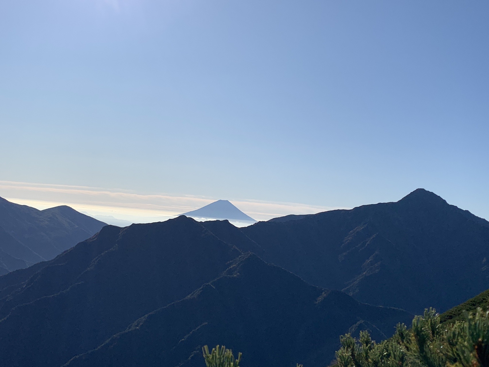 連なる山の稜線の向こう、雲海の上に富士山がくっきりと姿を現している