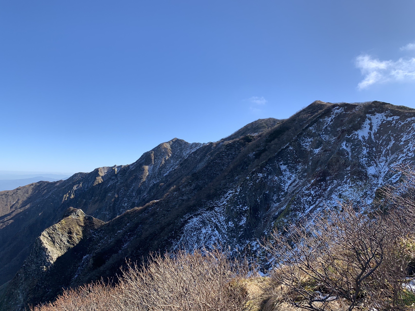 鋭く切れ落ちた岩の稜線。手前の斜面は崩れた岩肌がむき出しで、一部に雪が残っている
