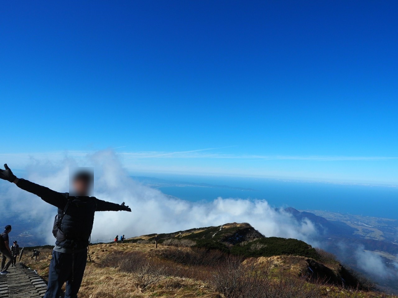 雲海を背に、稜線の上で両手を広げて立つ登山者