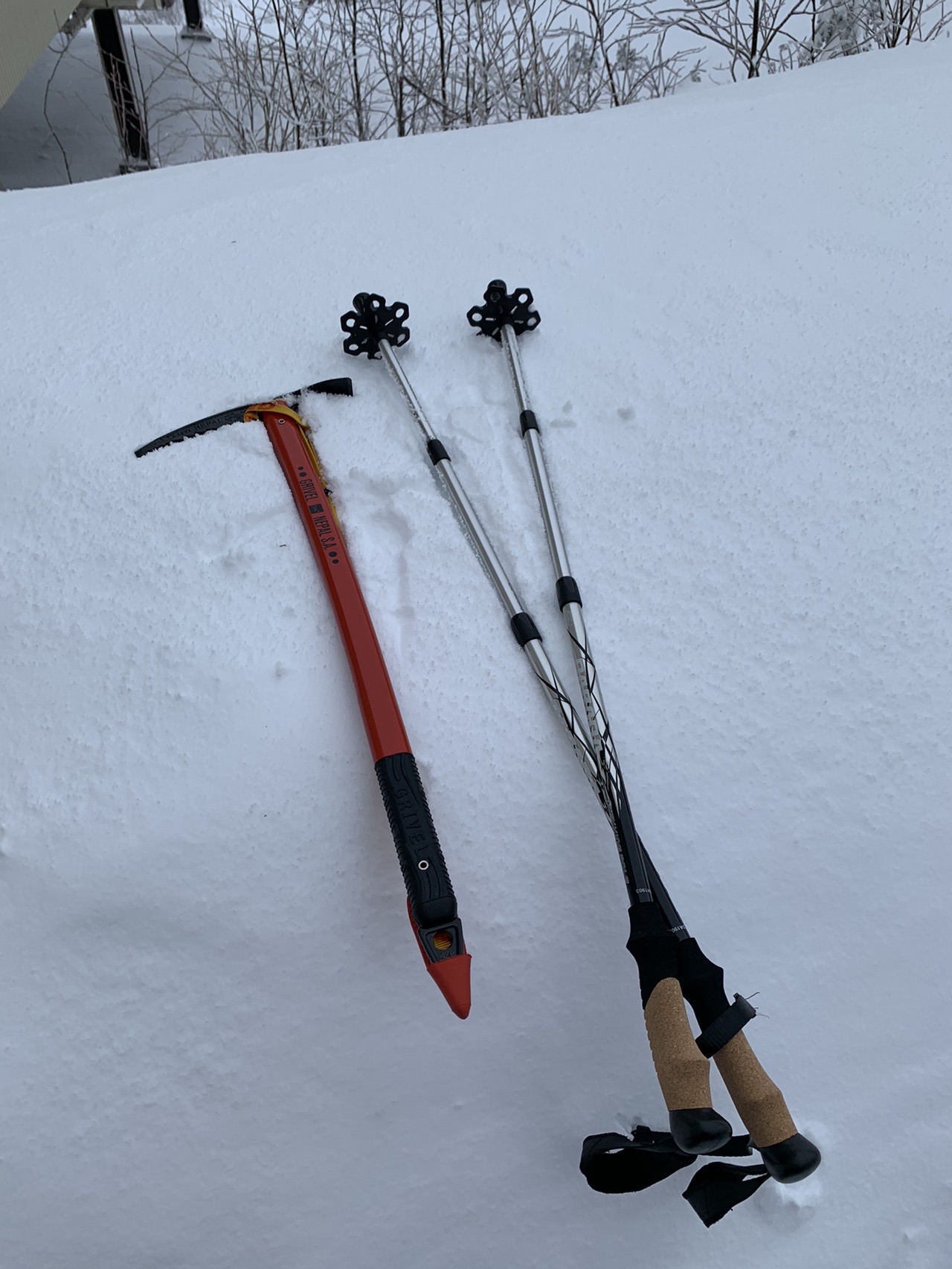 雪に突き刺さった赤いピッケルと2本のストック。周りは一面の雪