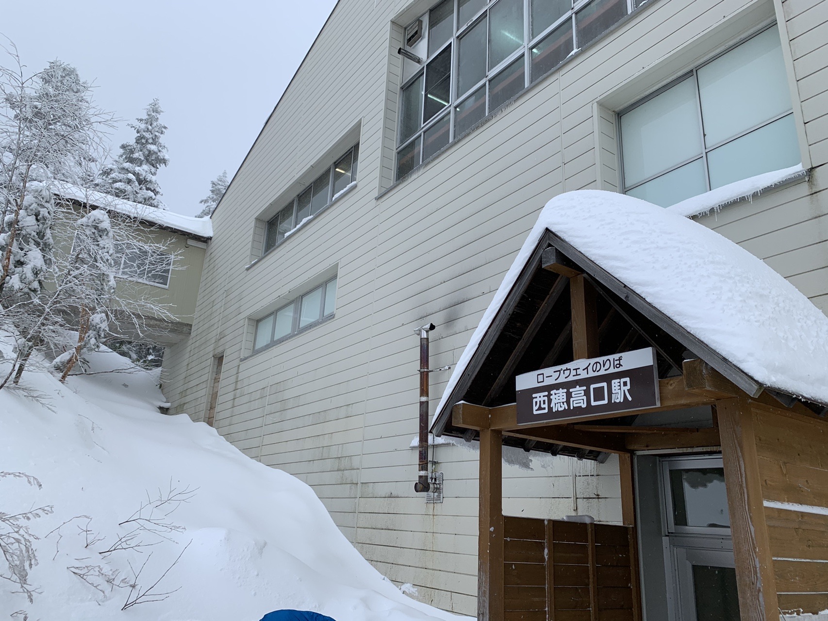 雪に半分埋まった西穂高口駅の建物。屋根にも壁際にも厚く雪が積もっている