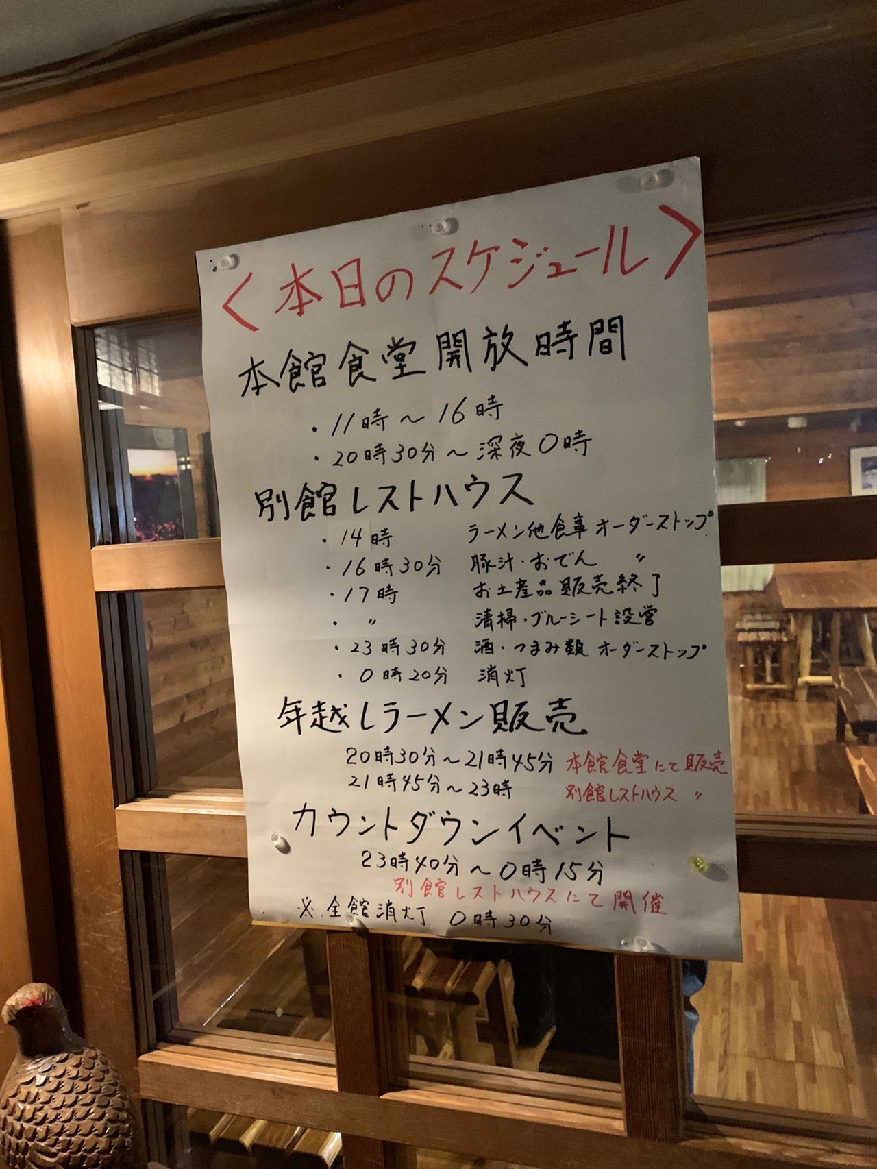 小屋の壁に貼られた手書きの掲示。「本日のスケジュール」と大きく書かれ、下に時間割が並んでいる