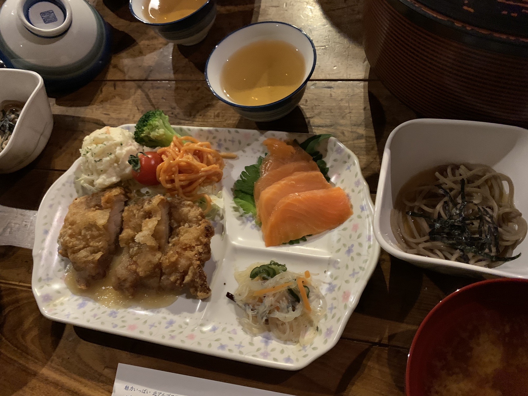 トレーに並んだ夕食。揚げた鶏肉、刺身、小鉢、味噌汁、ごはんが乗っている