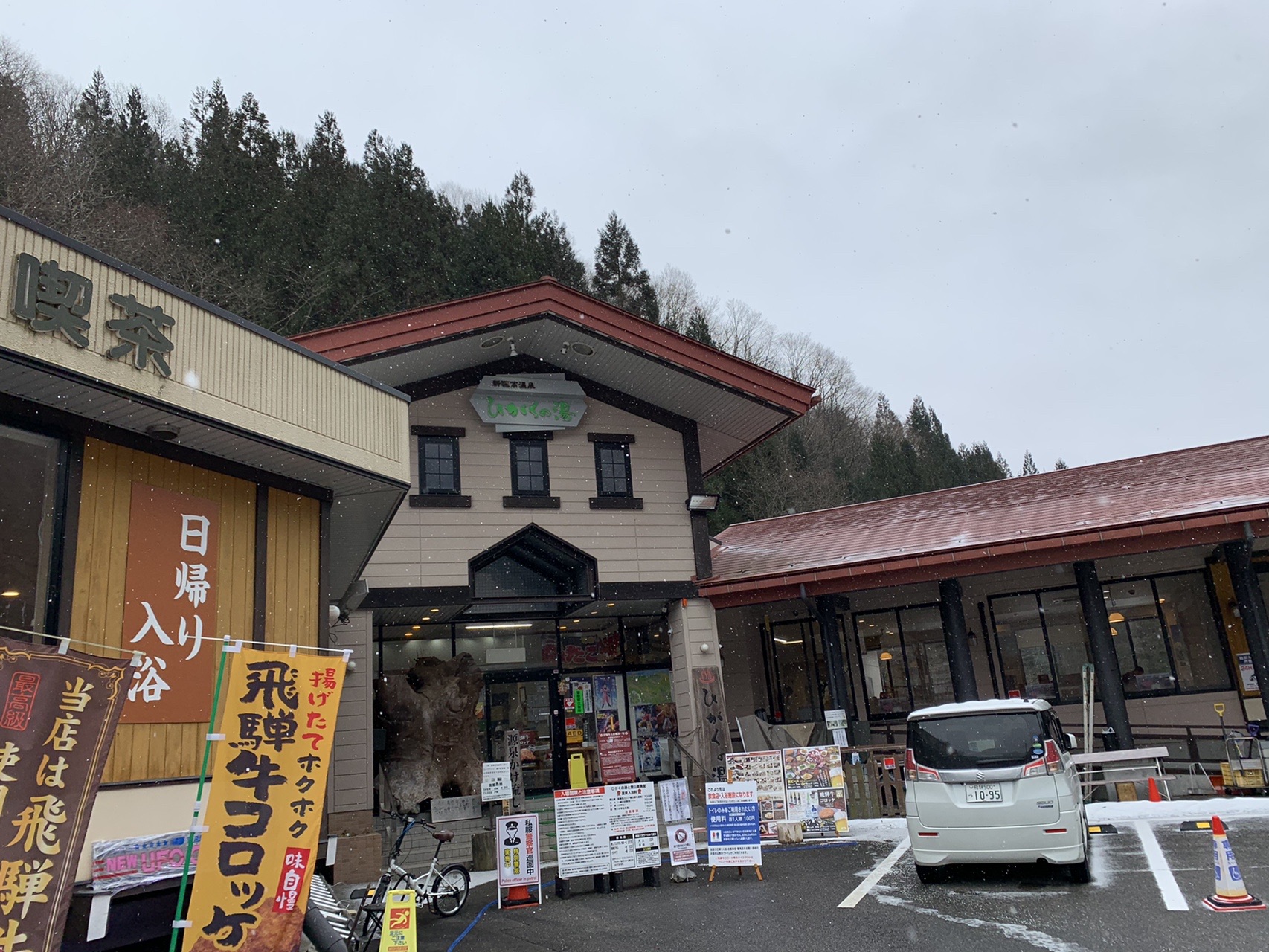 新穂高温泉の建物。「日帰り入浴」「飛騨牛コロッケ」ののぼりが立ち、前に車が停まっている