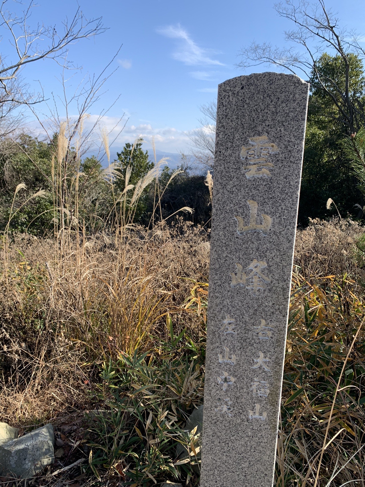 枯れ草の中に立つ細長い石柱。縦書きで「雲山峰」と刻まれている