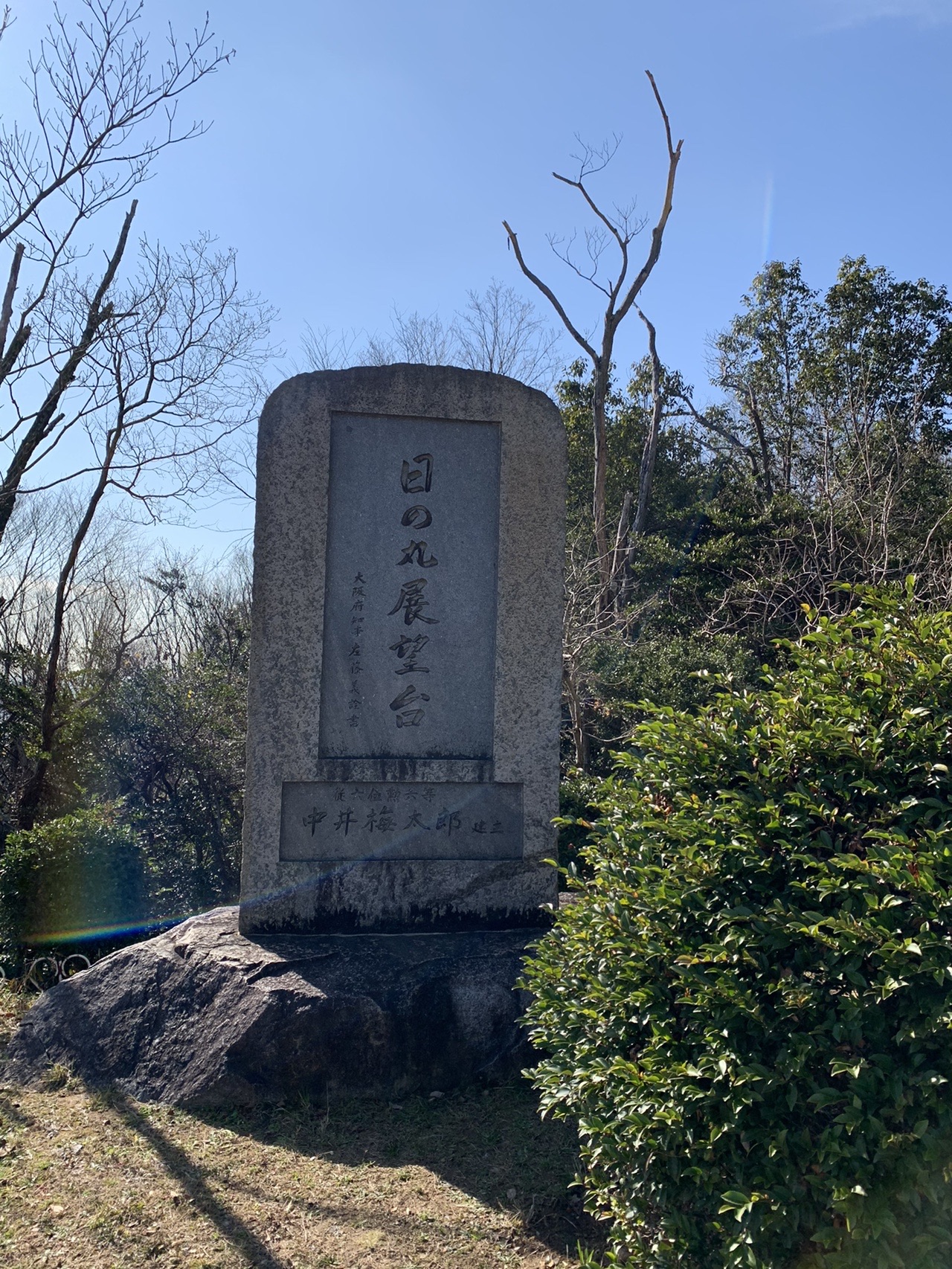 「日の丸展望台」と刻まれた背の高い石碑。青空と裸の木が背景に見える