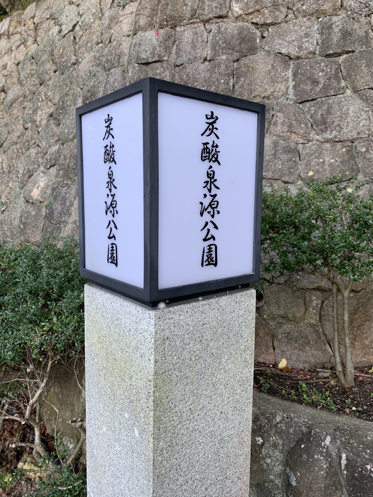 石の柱に「炭酸泉源公園」と刻まれた石碑。上部に四角い灯りが乗っている