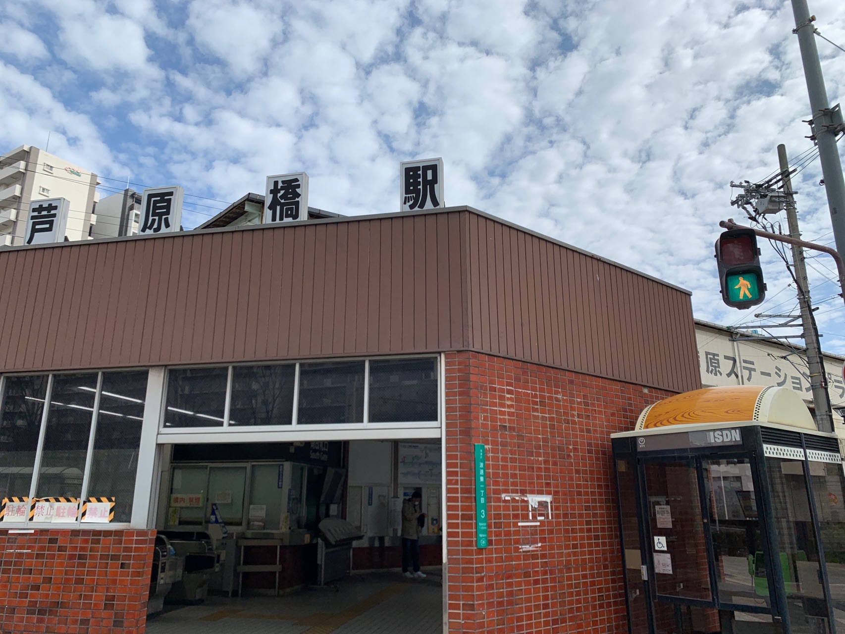 レンガ色の壁の芦原橋駅の駅舎。上部に「芦原橋駅」と大きく書かれ、うろこ雲が広がる空が見える