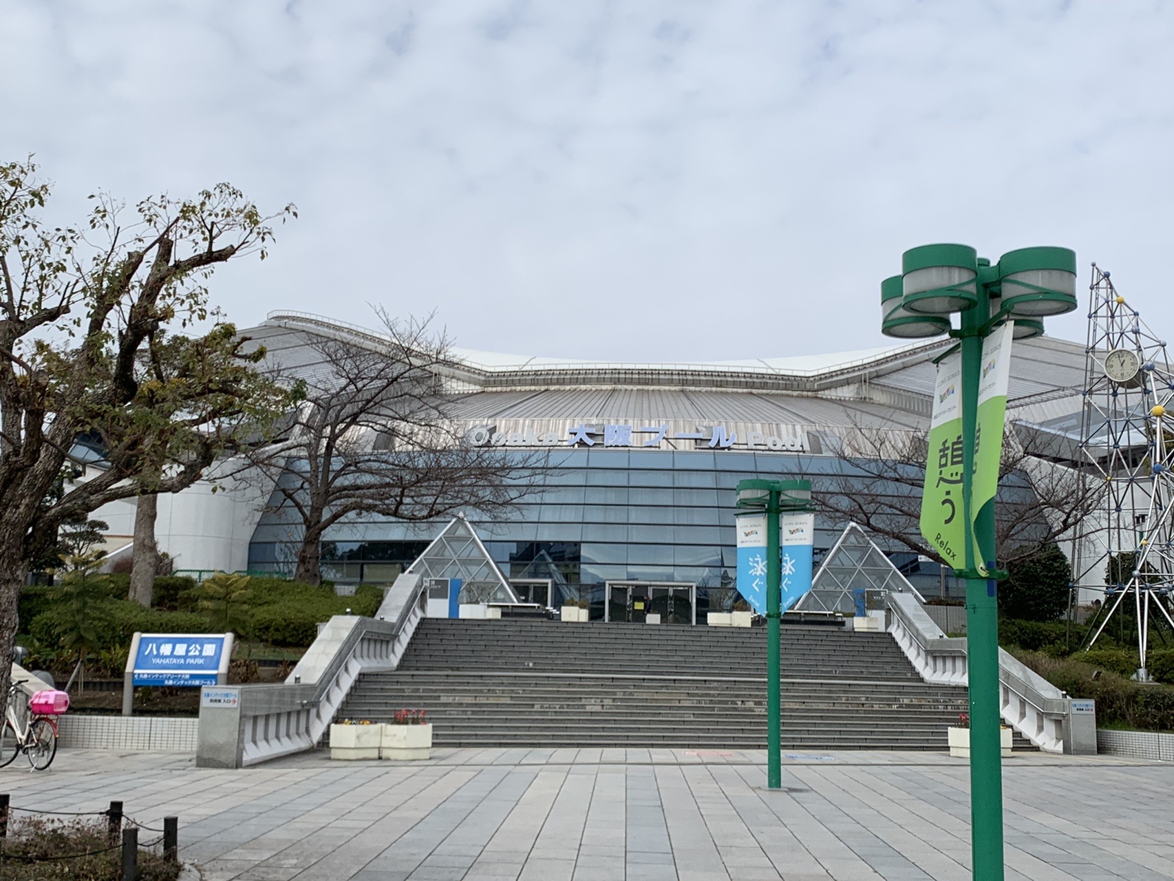八幡屋公園の広い階段と、その先に建つ大きなドーム状の屋根の体育施設。緑の街灯が並ぶ