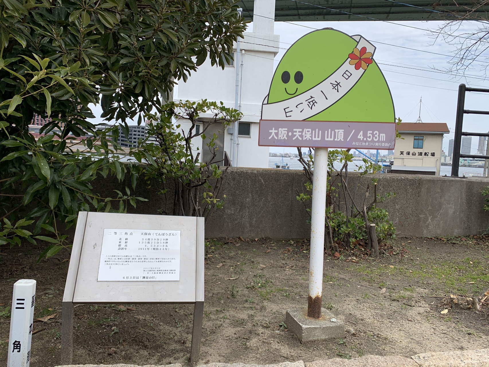 緑色の山の形をしたキャラクター看板。「日本一低い山」のたすきをかけ、下に「大阪・天保山 山頂 / 4.53m」と書かれている。左手前に三角点の説明板