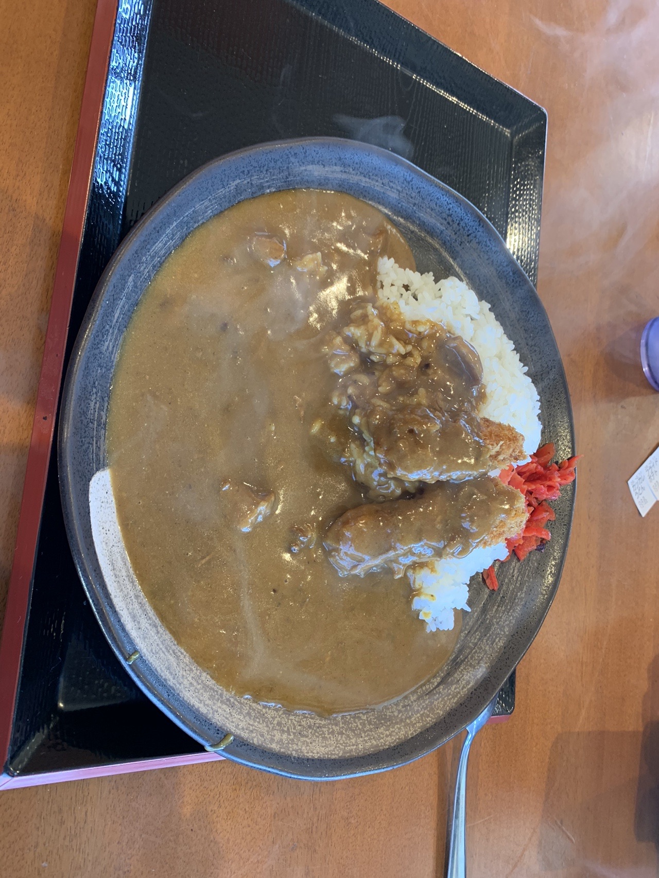 大きな平皿に盛られたカツカレー。たっぷりのルーの上に福神漬けが添えられている