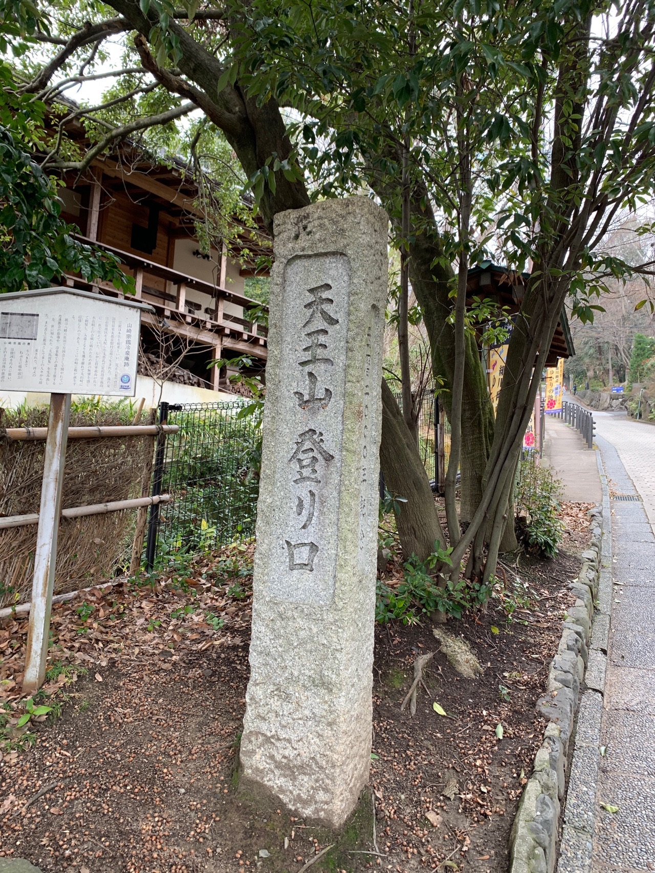 舗装路のわきに立つ古い石柱。「天王山 登り口」と刻まれている。奥に民家の屋根