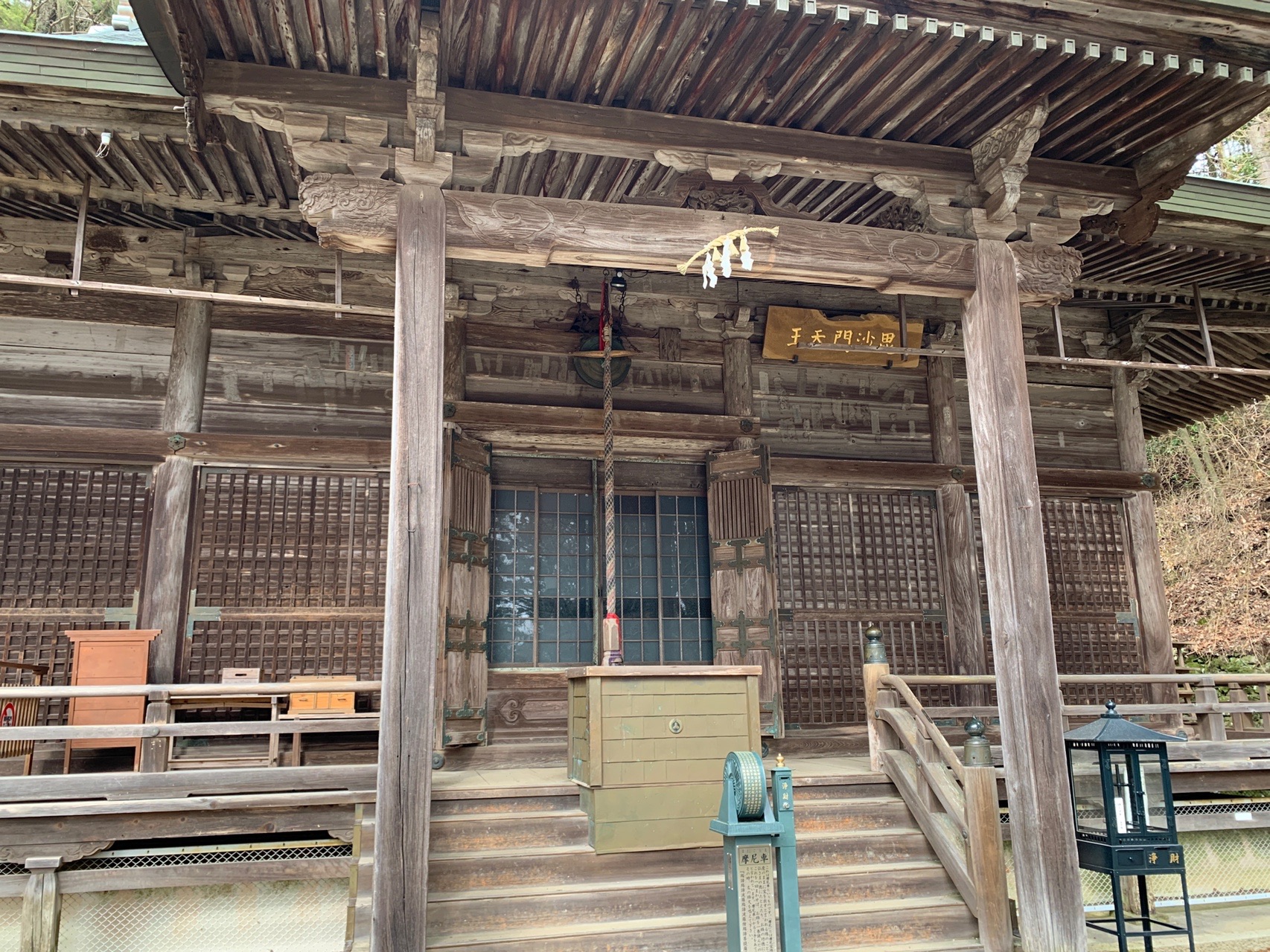 木造のお堂の正面。格子戸と縁側があり、軒下に扁額が掛かっている