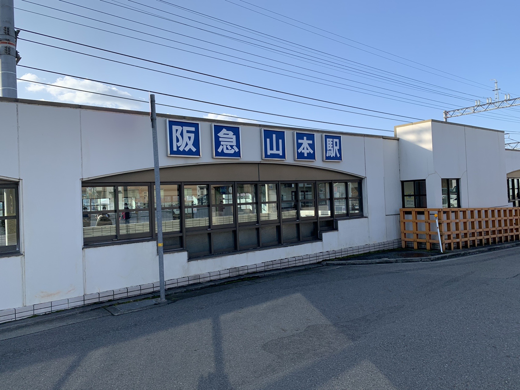 阪急山本駅の白い駅舎。青空の下、駅前のロータリーが広がっている