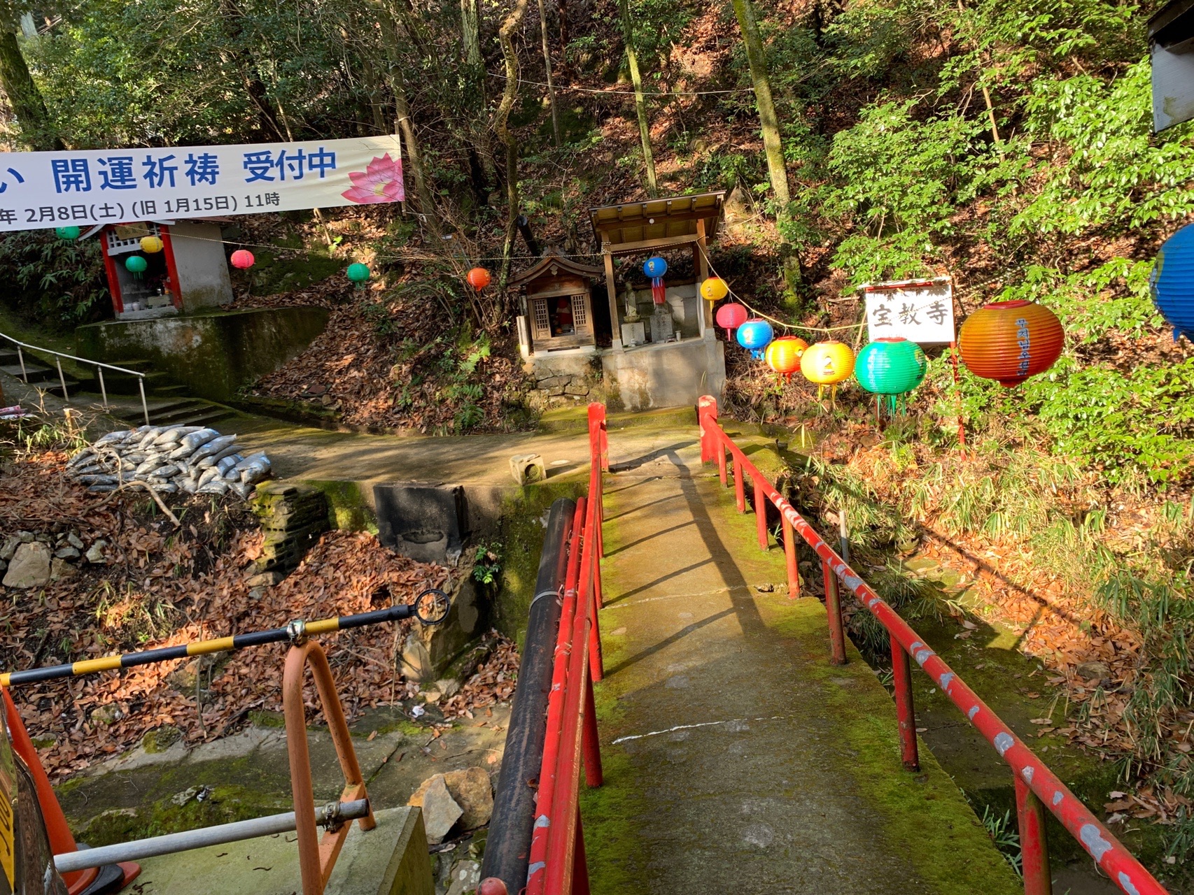 赤い欄干の橋と、カラフルな提灯が並んだ参道。奥に「開運祈祷 受付中」の幟が立っている