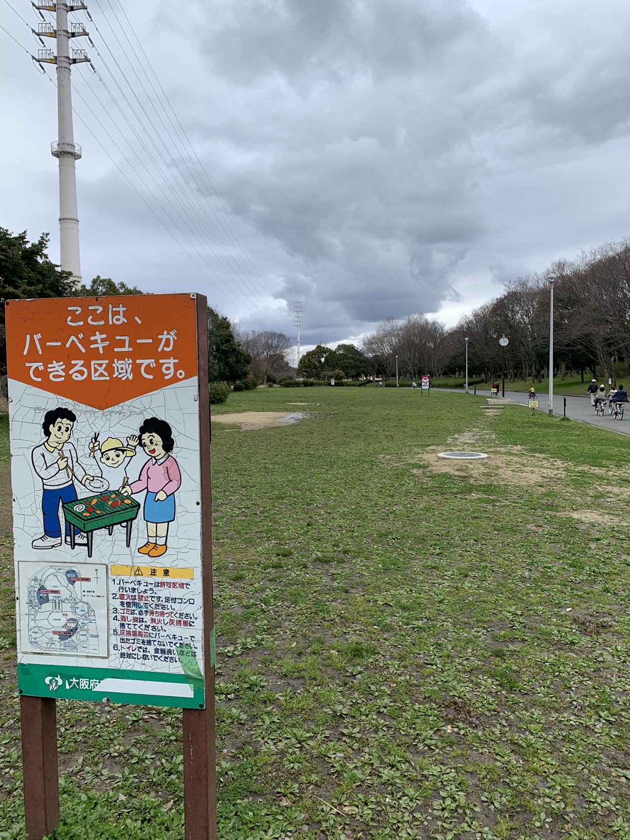 バーベキューができる区域を示す看板。奥に広い芝生と木立が広がっている