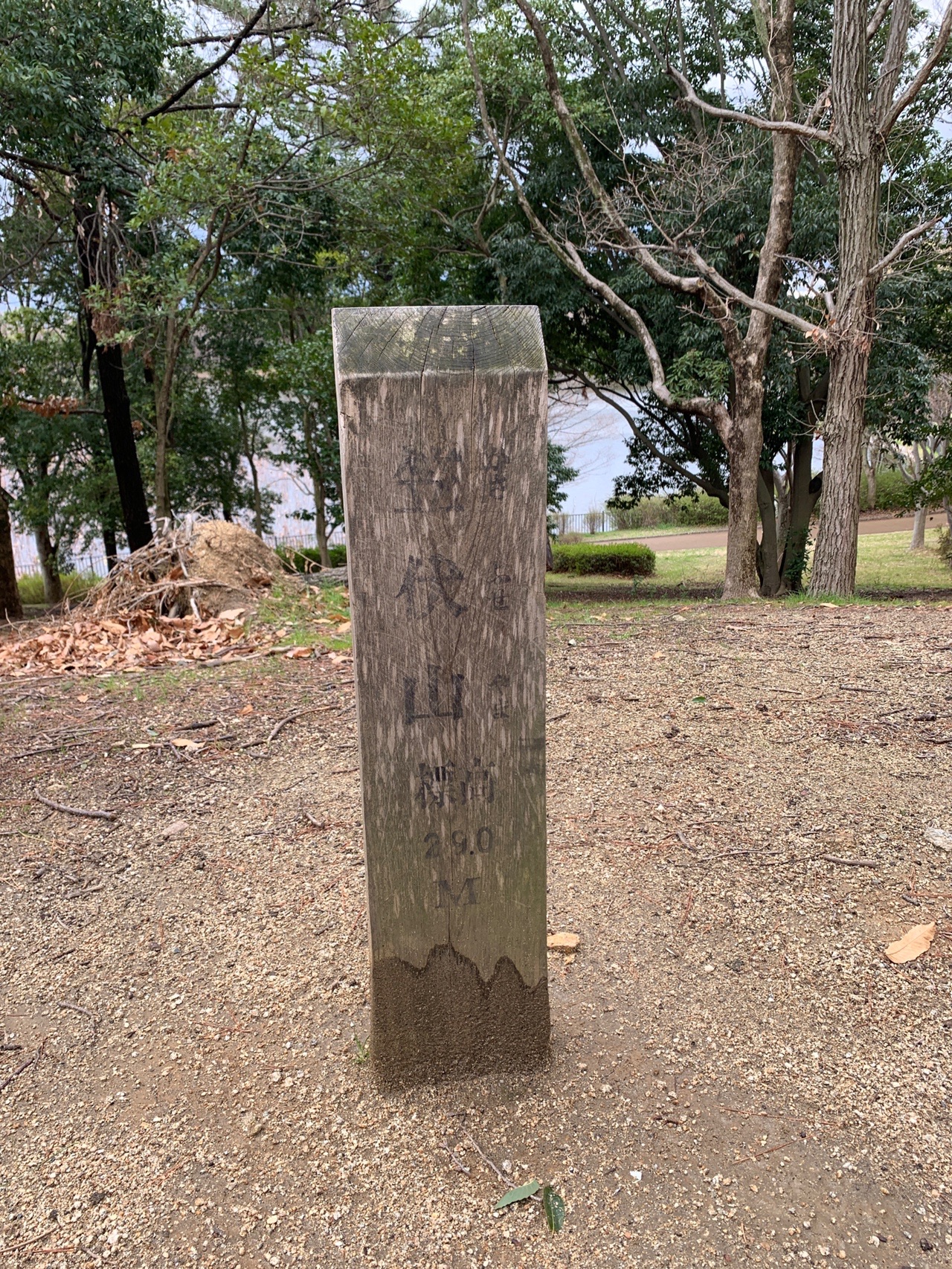 「笠伏山 標高29.0M」と彫られた木の標柱。奥に池が見える