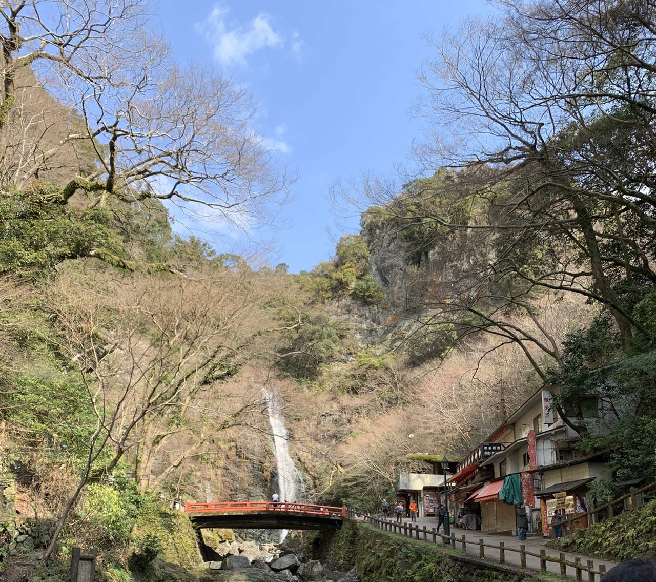 谷の奥に落ちる箕面大滝。手前に赤い橋と、滝への遊歩道沿いに並ぶ店が見える