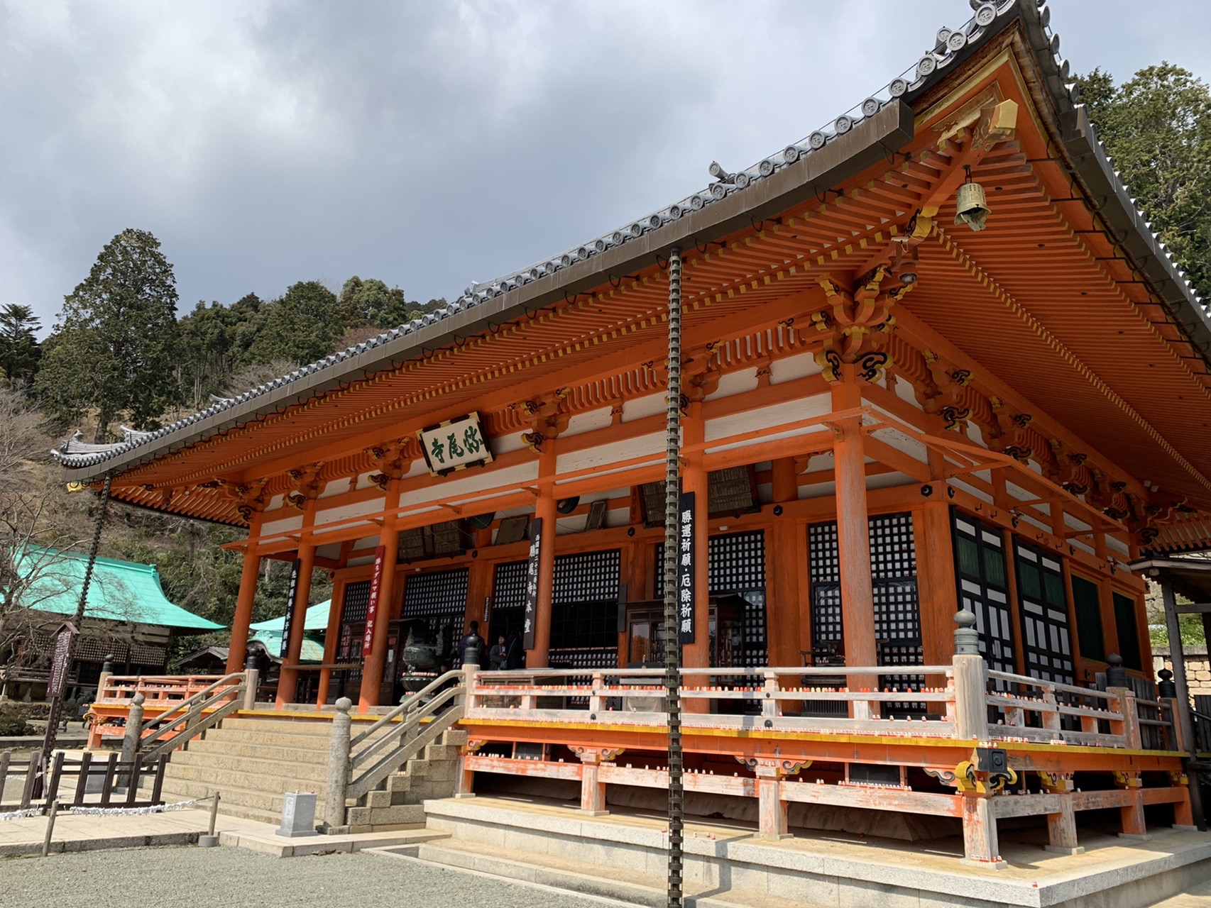 勝尾寺の朱塗りの本堂。曇り空の下、山の斜面に建っている