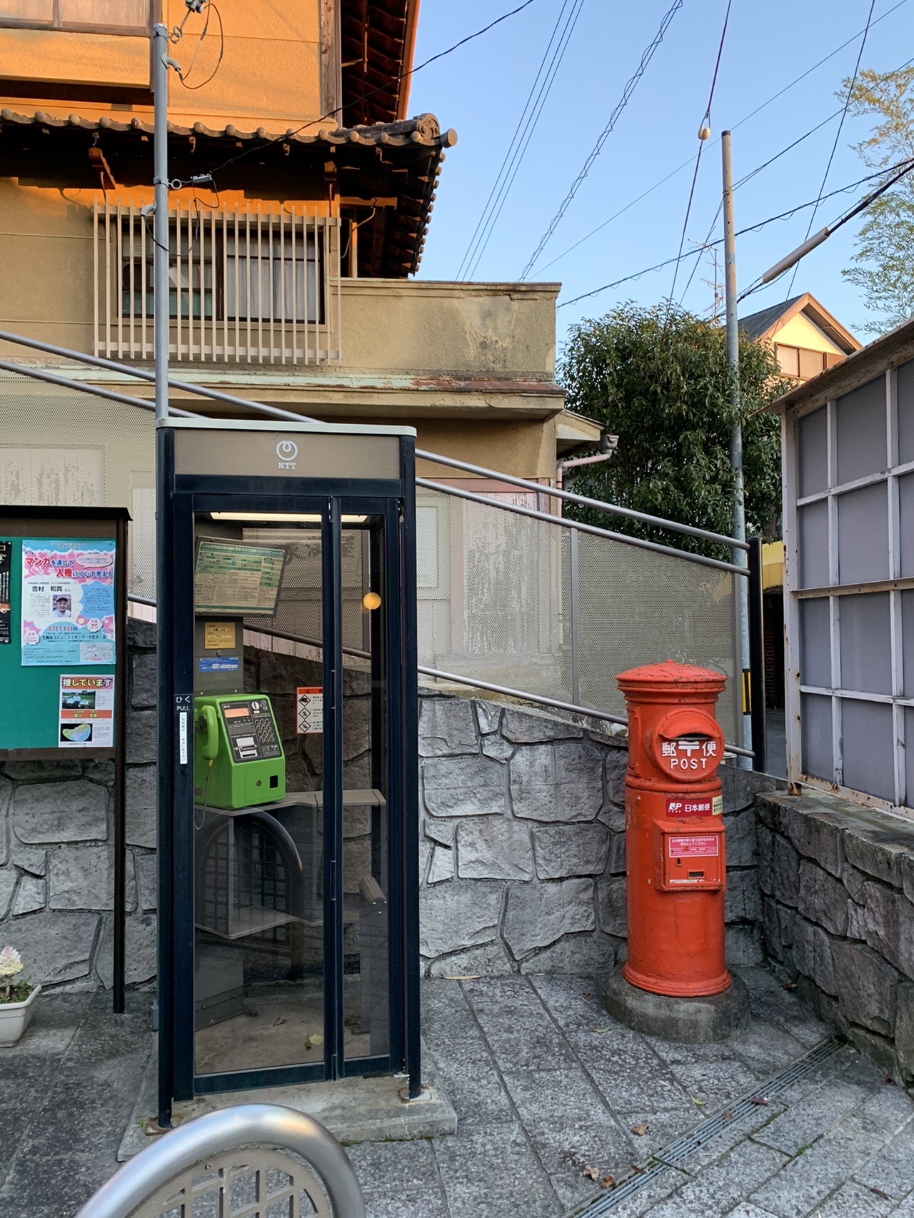 道端に並んで立つ緑色の公衆電話ボックスと赤い丸型ポスト。朝の光が当たっている