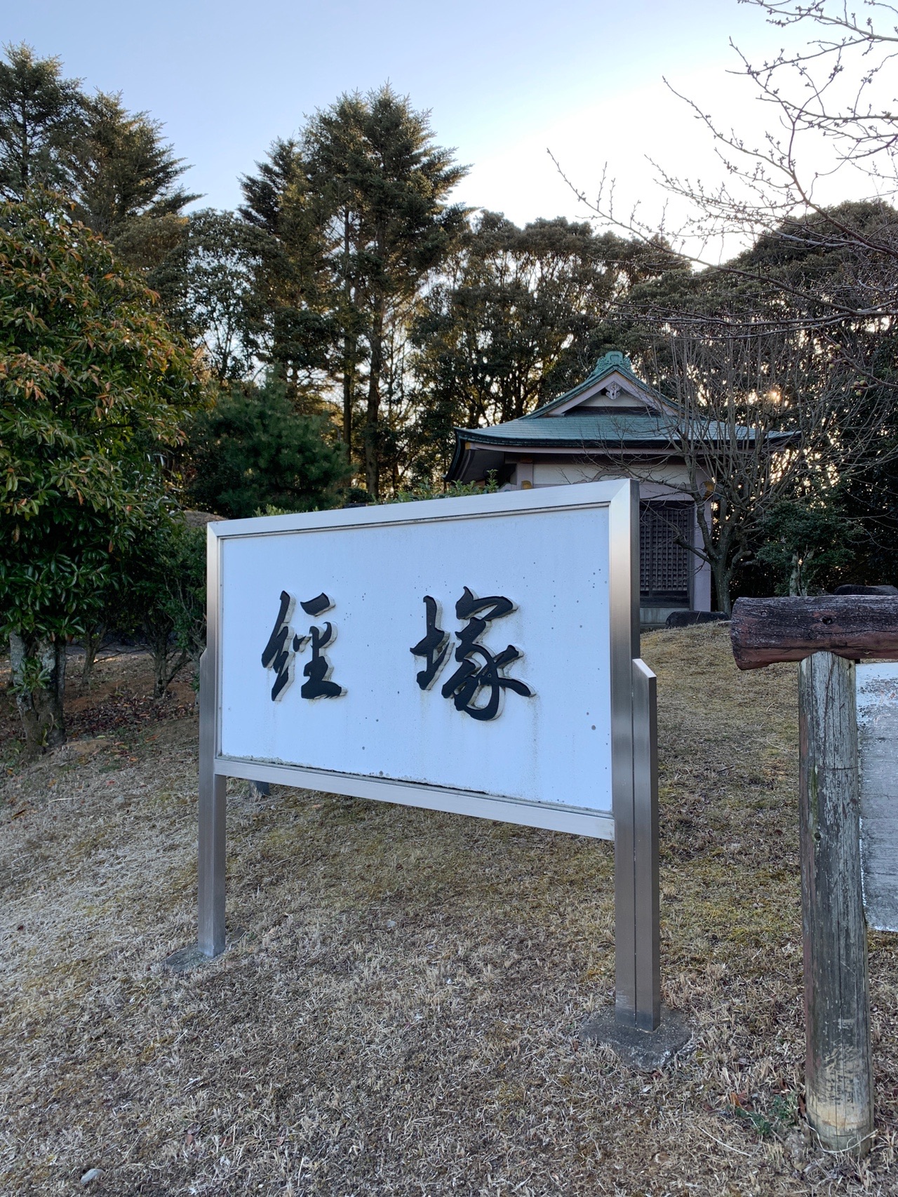 「経塚」と刻まれた白い石碑。奥に緑色の屋根の小さなお堂が建っている