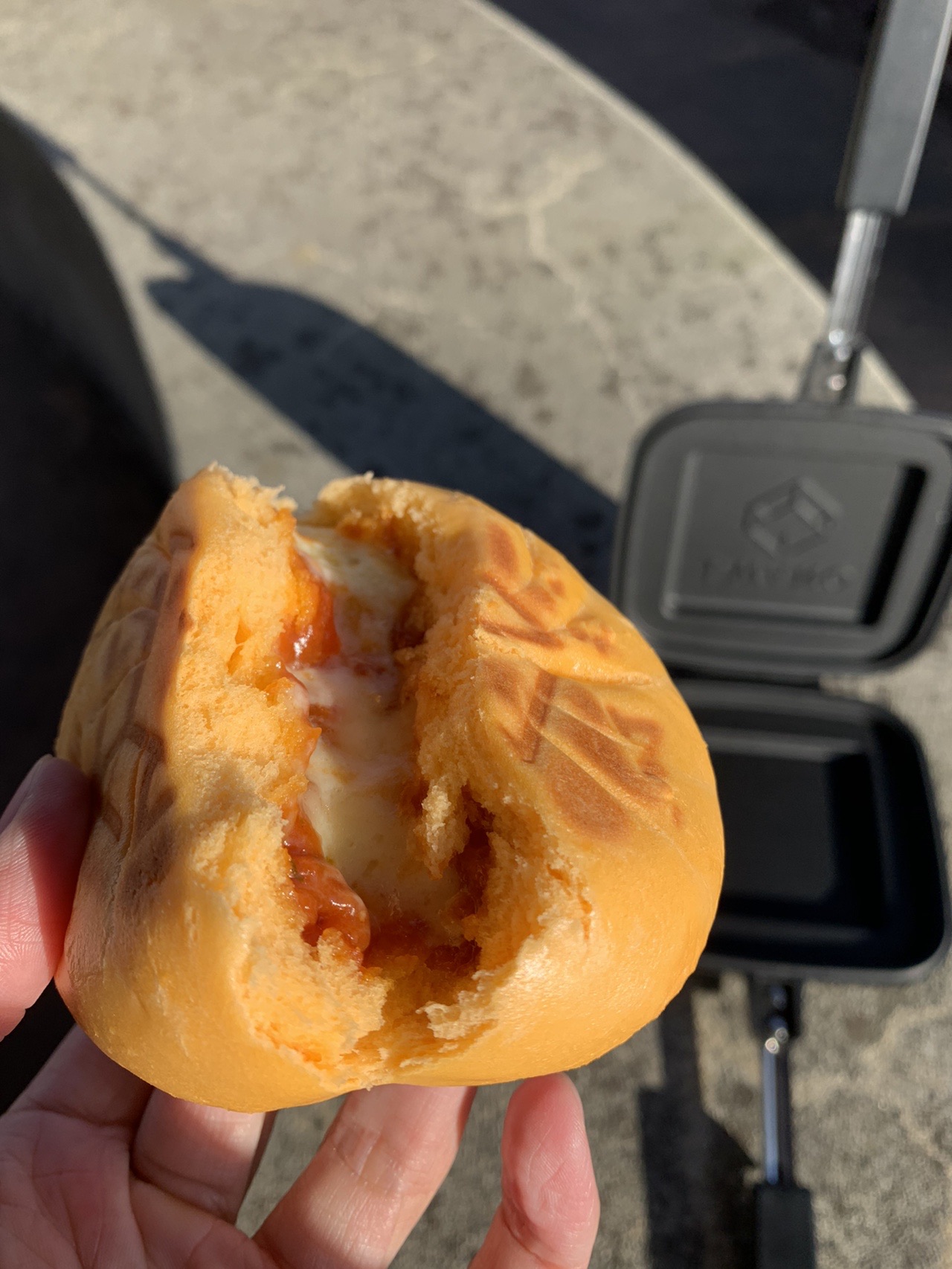 手に持った焼き目のついたピザまん。表面に花のような焼印がついている