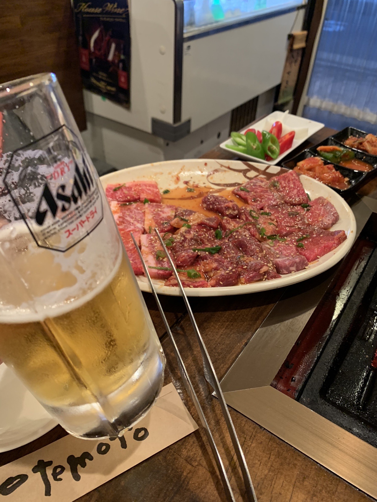 焼肉店のテーブル。生ビールのジョッキと、赤身肉が盛られた皿