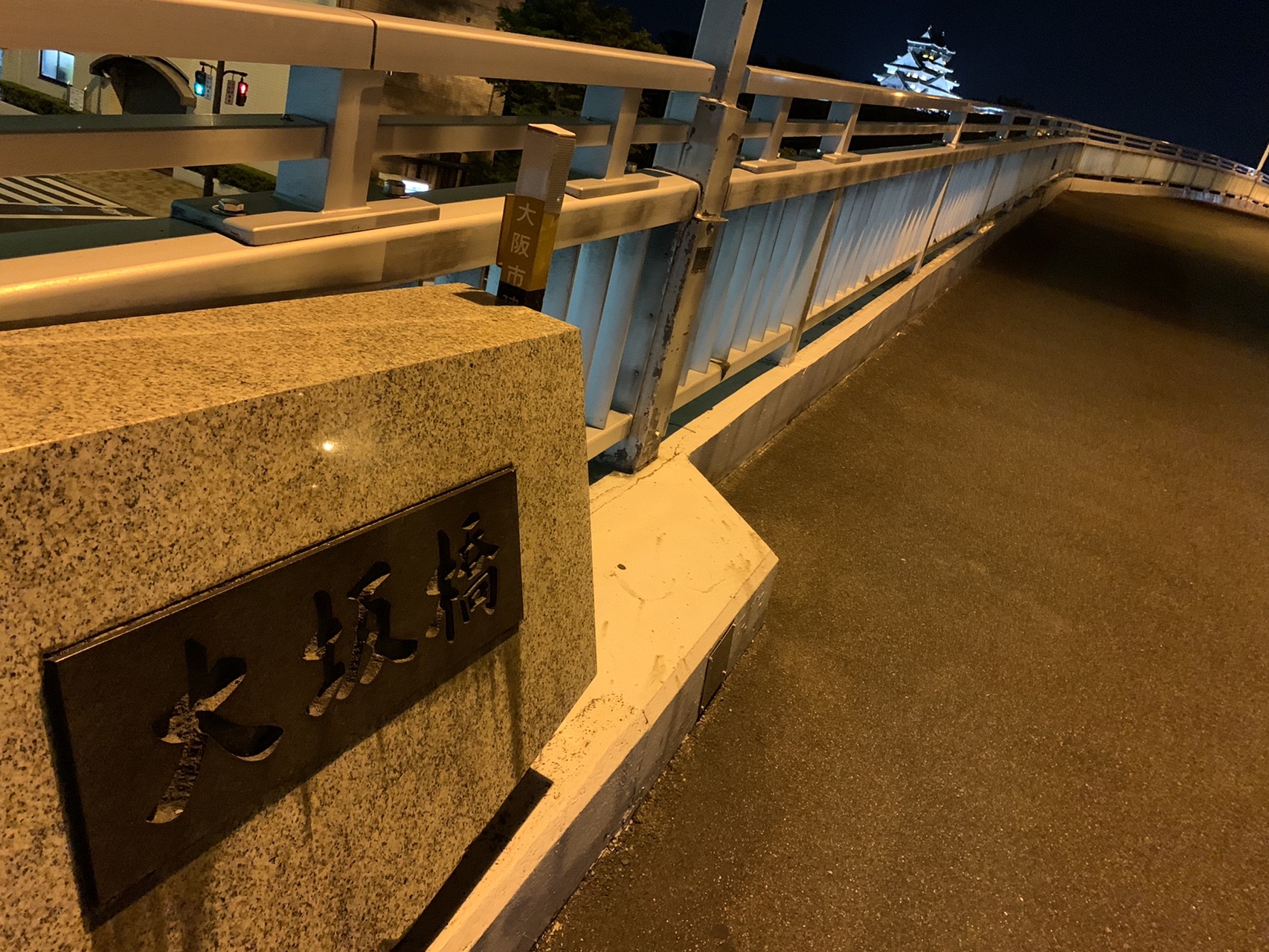 橋の親柱に「大坂橋」の銘板。橋の向こうにライトアップされた大阪城が小さく見える