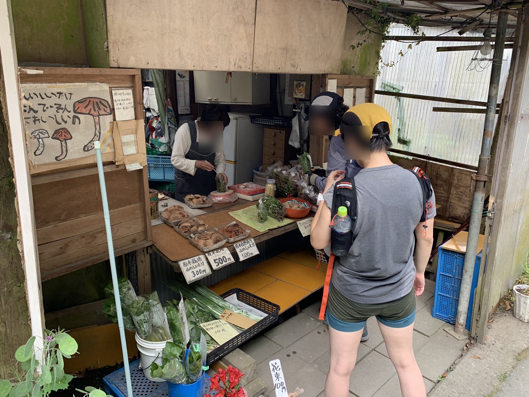 山道沿いの小屋で、木の台に原木しいたけのパックが並ぶ直売所。プライバシー保護のため顔にぼかしを入れています