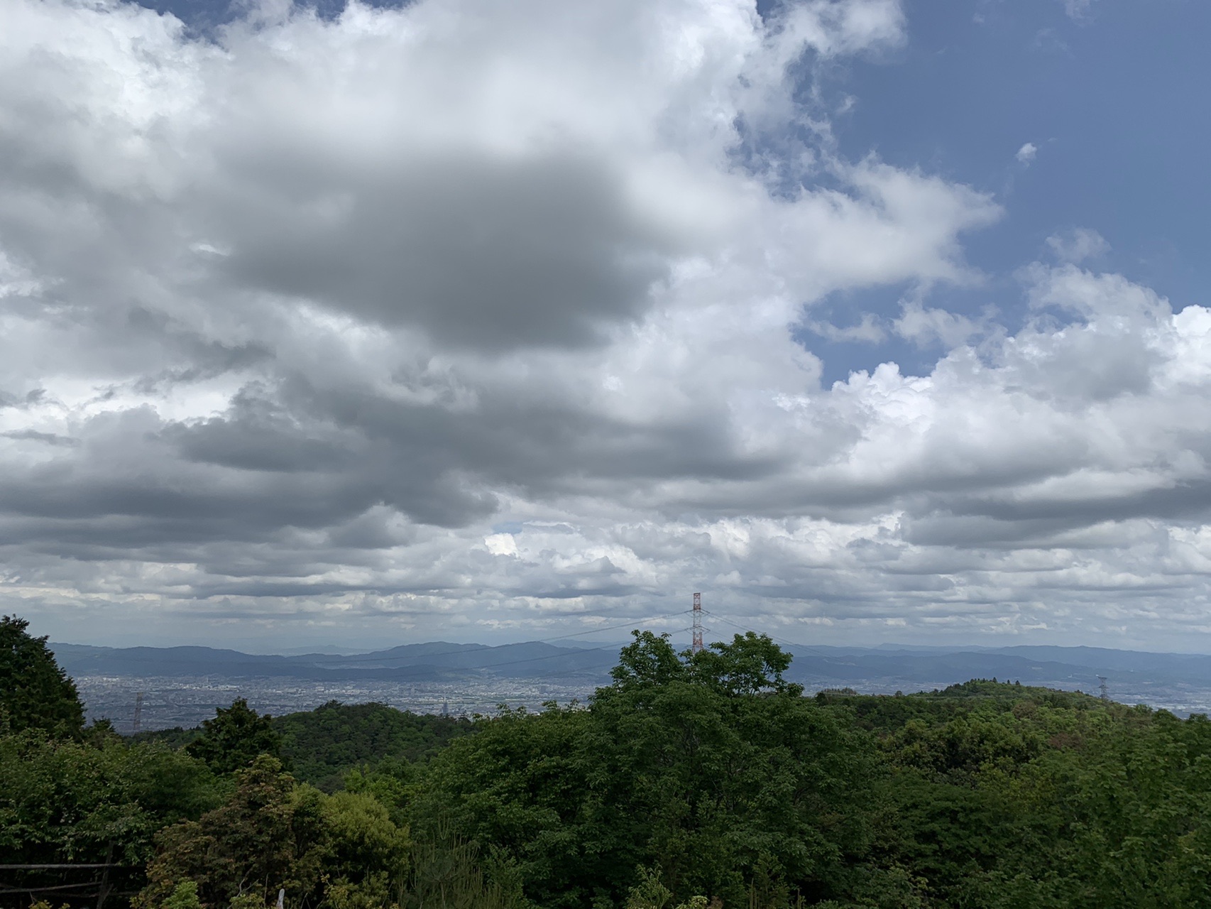 ポンポン山の山頂から見た、雲の多い空と遠くまで広がる山並みと街