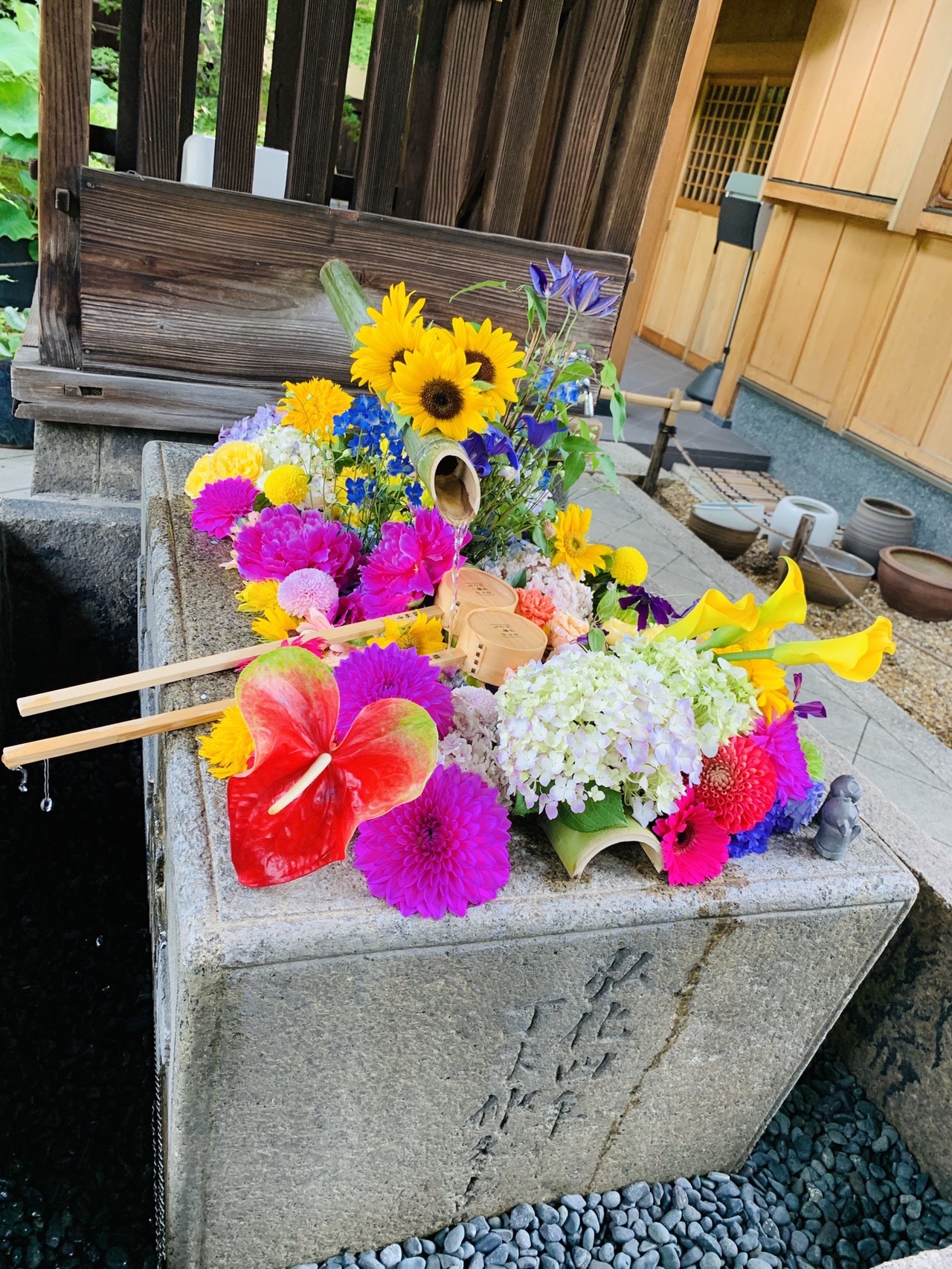 石の手水鉢に、黄色・赤・紫など色とりどりの花が浮かべられている