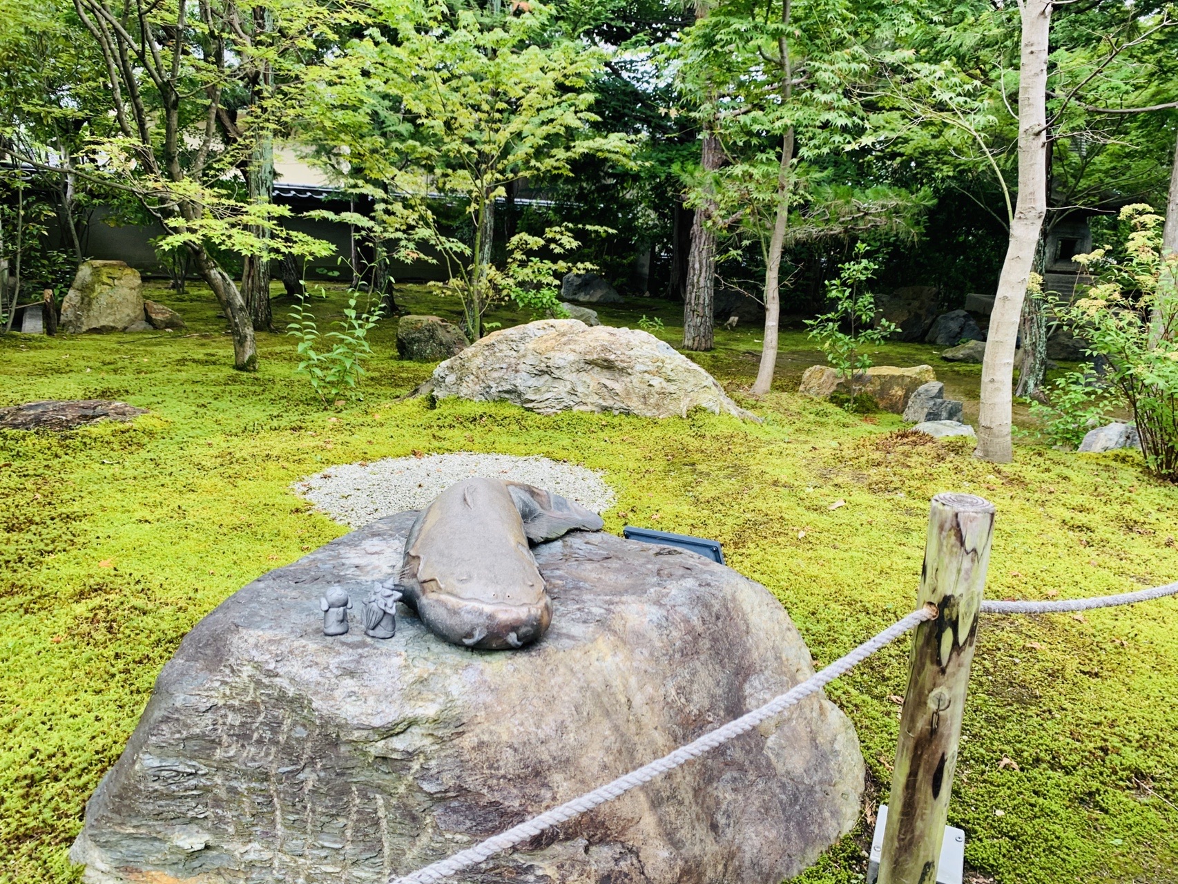苔むした庭の大きな石の上に置かれた、なまずをかたどった石の彫刻