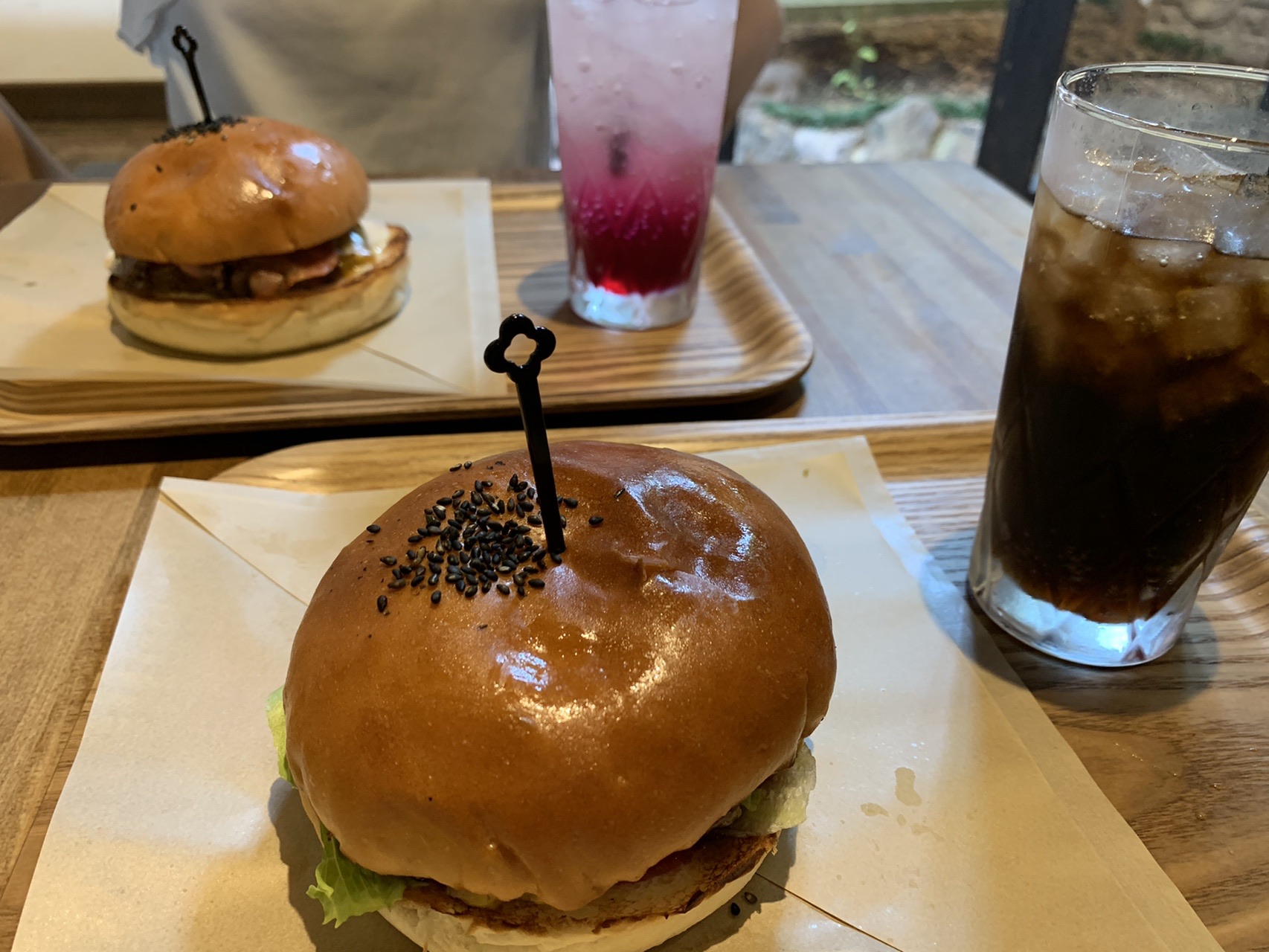 木のトレーにのった、つやのあるバンズのハンバーガーと、アイスコーヒーとソーダ