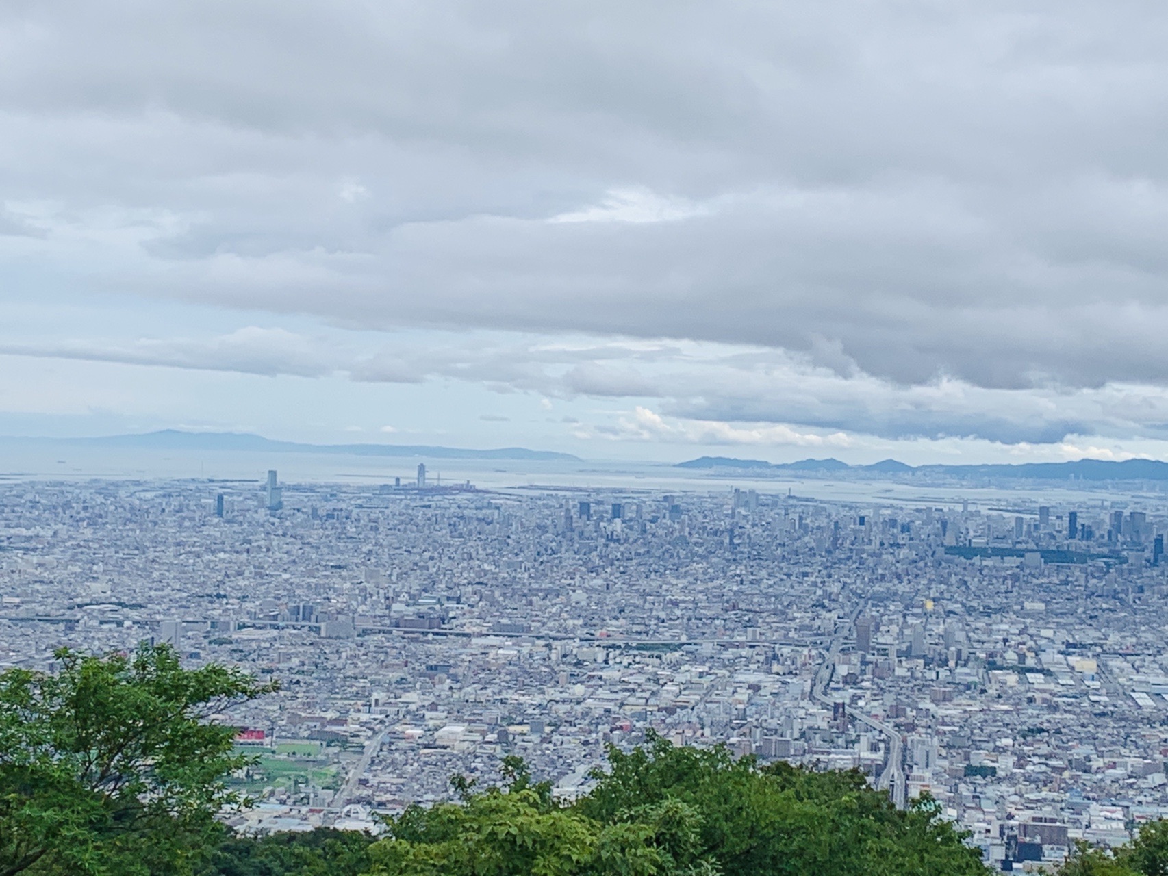厚い雲の下に大阪平野が広がり、その先に淡路島と明石海峡大橋が見える