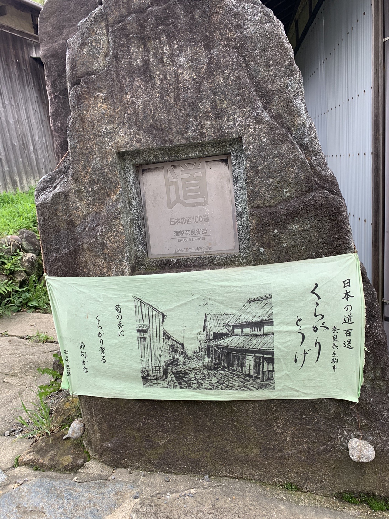 「くらがり峠」と書かれた幟と、石に埋め込まれた日本の道百選の顕彰碑